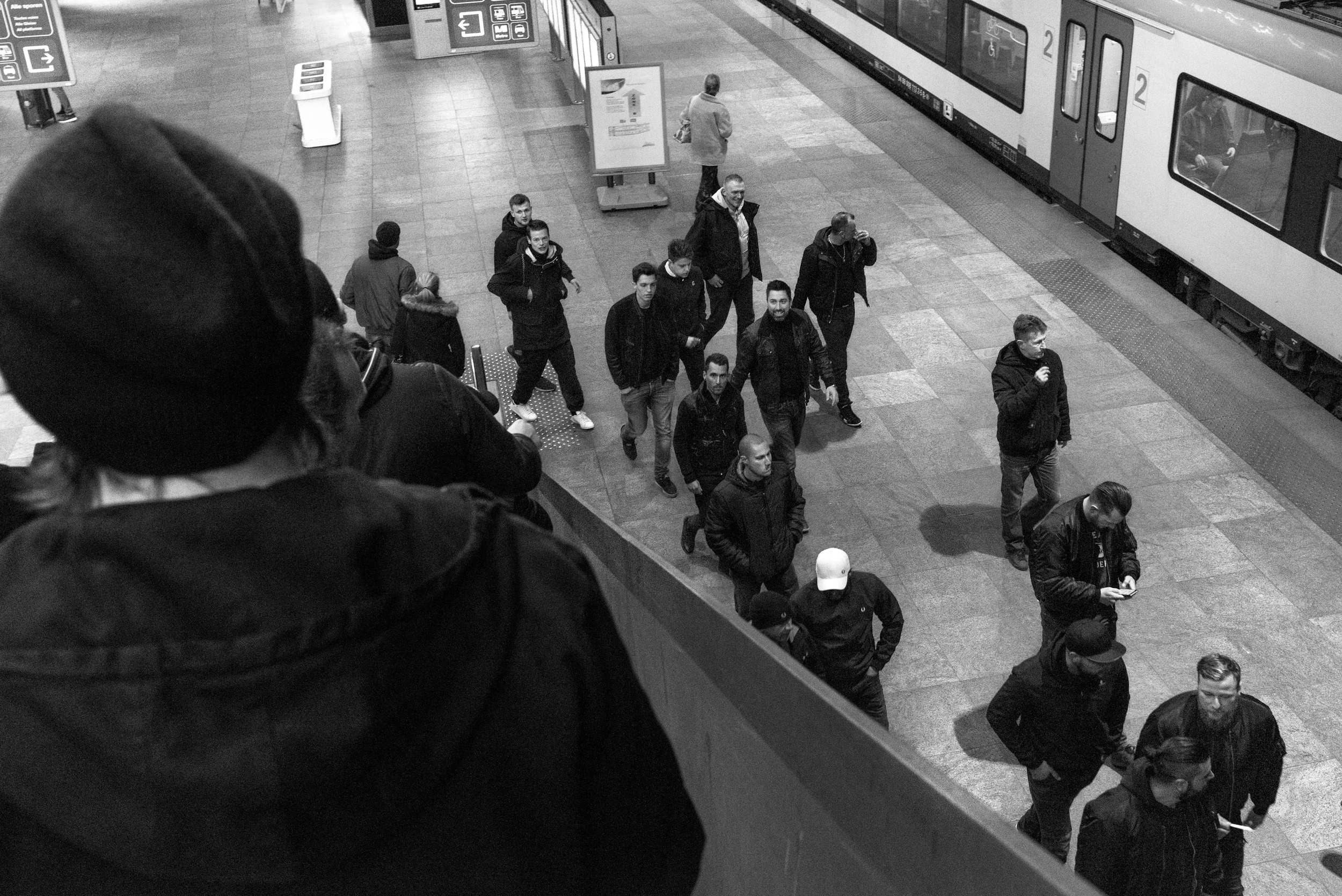 Een zwart-wit foto van een disturbatrice die mensen op een trein onderaan de escalator observeert in een station.