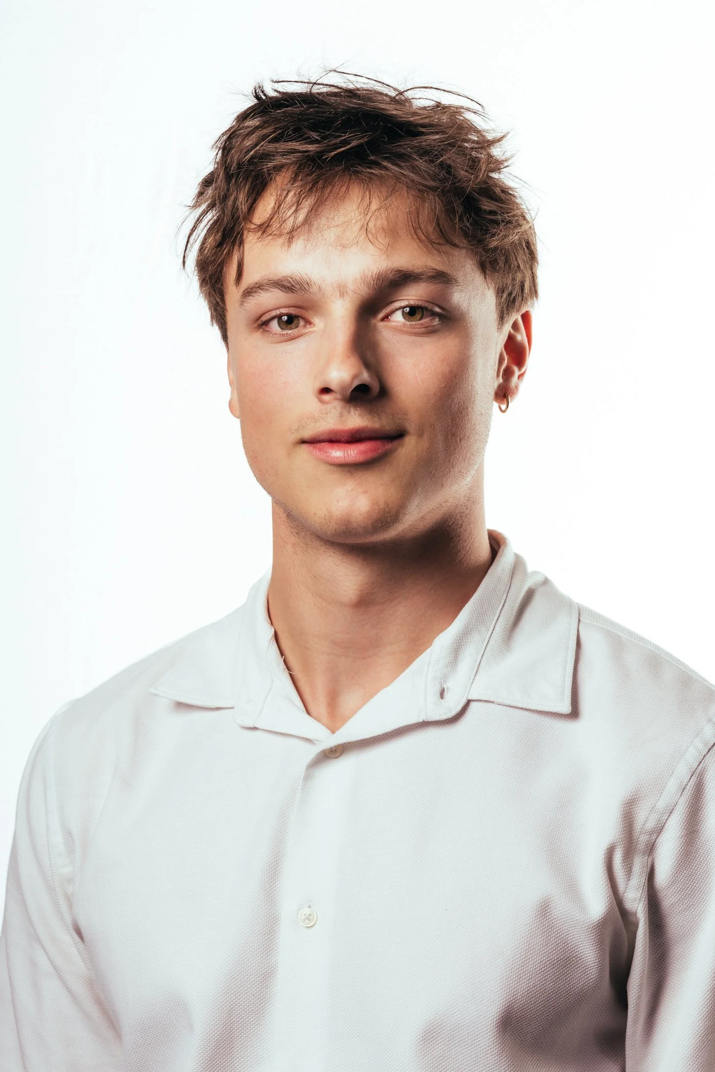 Portret van een jonge man met kort, wirwarig haar, die een witte blouse draagt, lachend op een witte achtergrond.