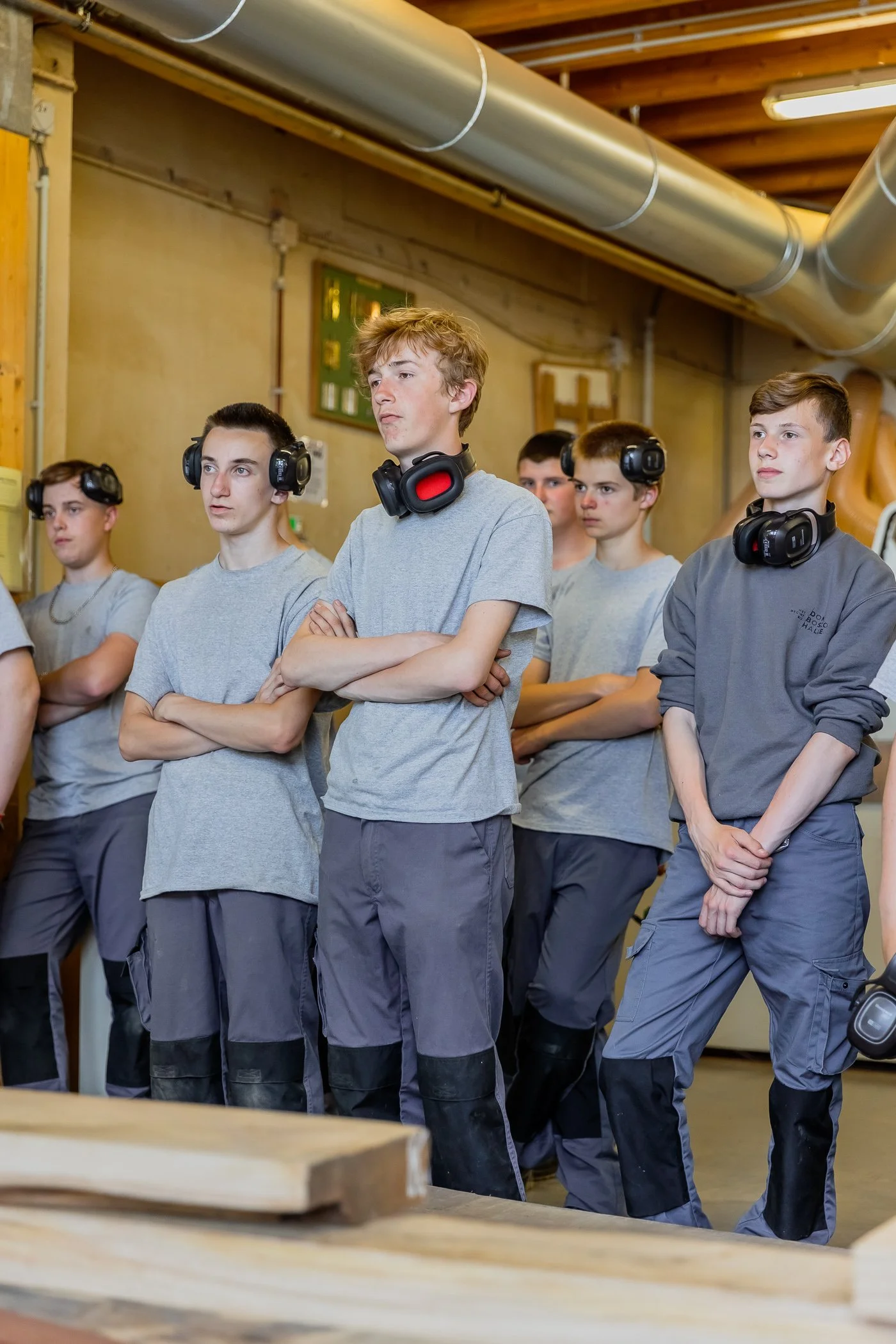 Een groep jongens in een werkplaats, allemaal met koptelefoons om, luisteren aandachtig naar iets dat buiten beeld is.