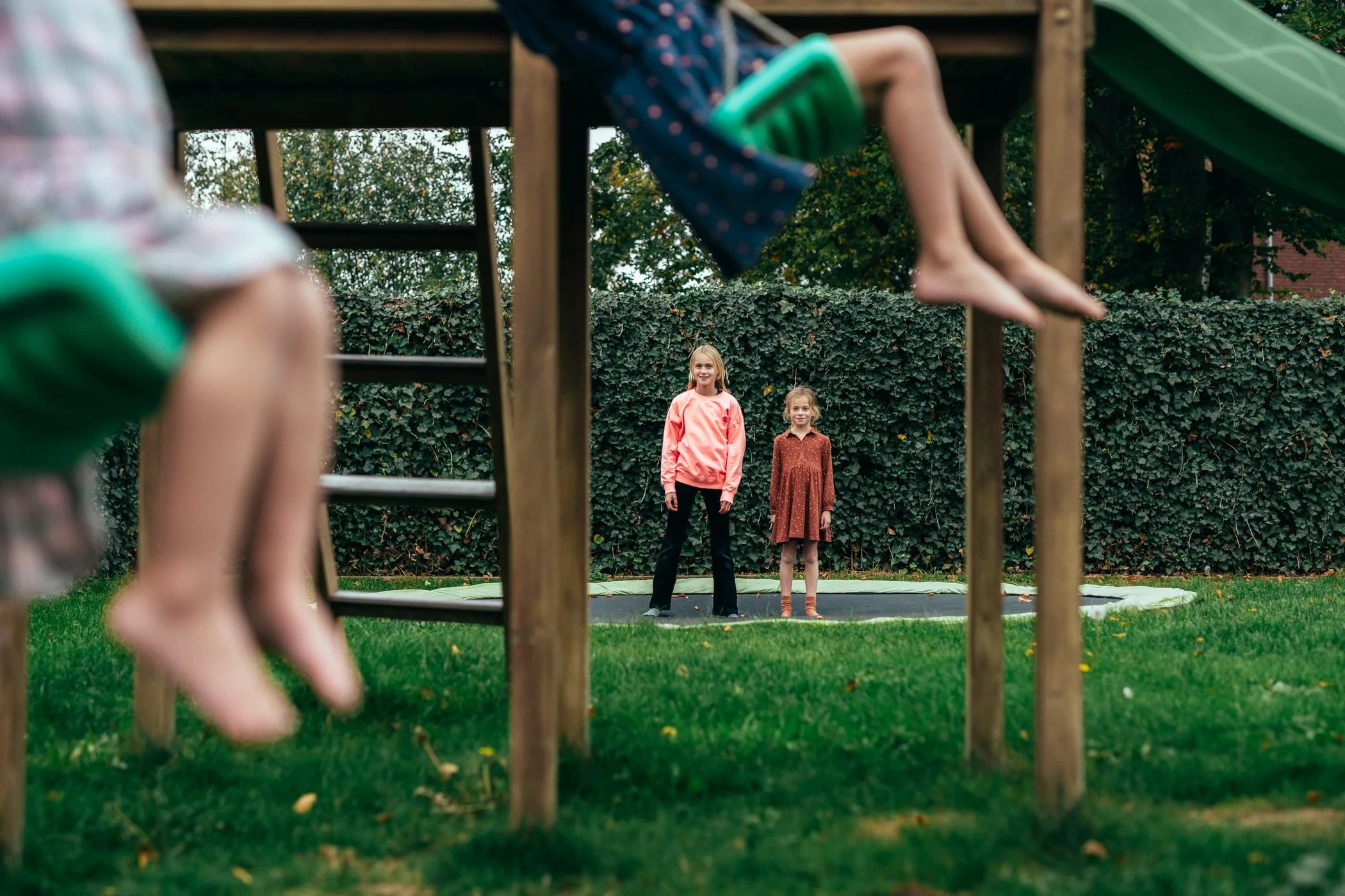 Twee meisjes op een trampoline, gezien vanuit onder de speeltoestellen in de tuin.