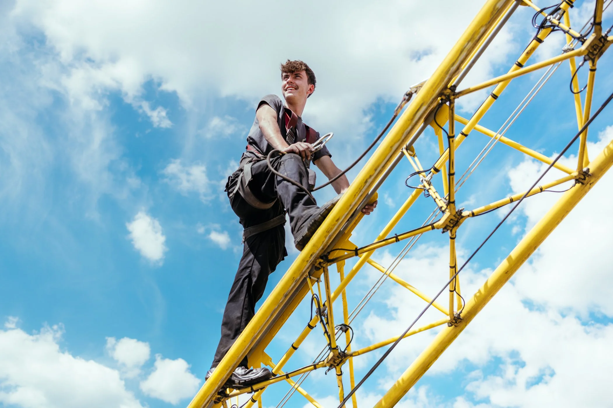 Man op een gele toren klimt, blauwe lucht met wolken op de achtergrond.