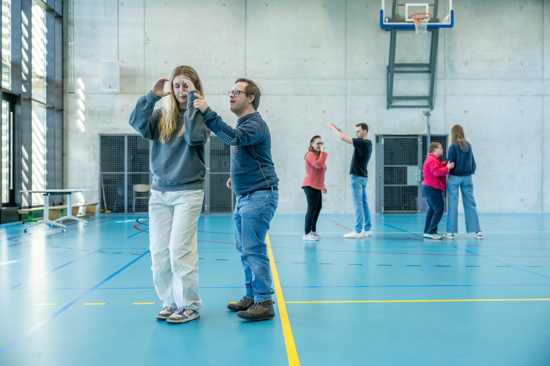 Een gymzaal met twee paren, waarbij het ene paar elkaar niet lijkt te begrijpen en het andere paar dicht bij elkaar staat.