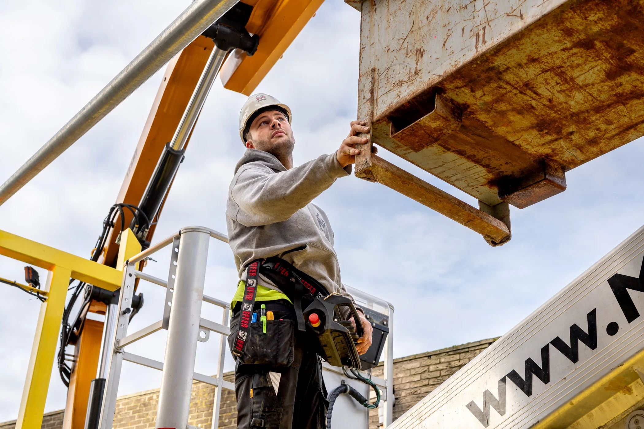 Bouwvakker in veiligheidskleding en helm bedient hoogwerker op bouwplaats.