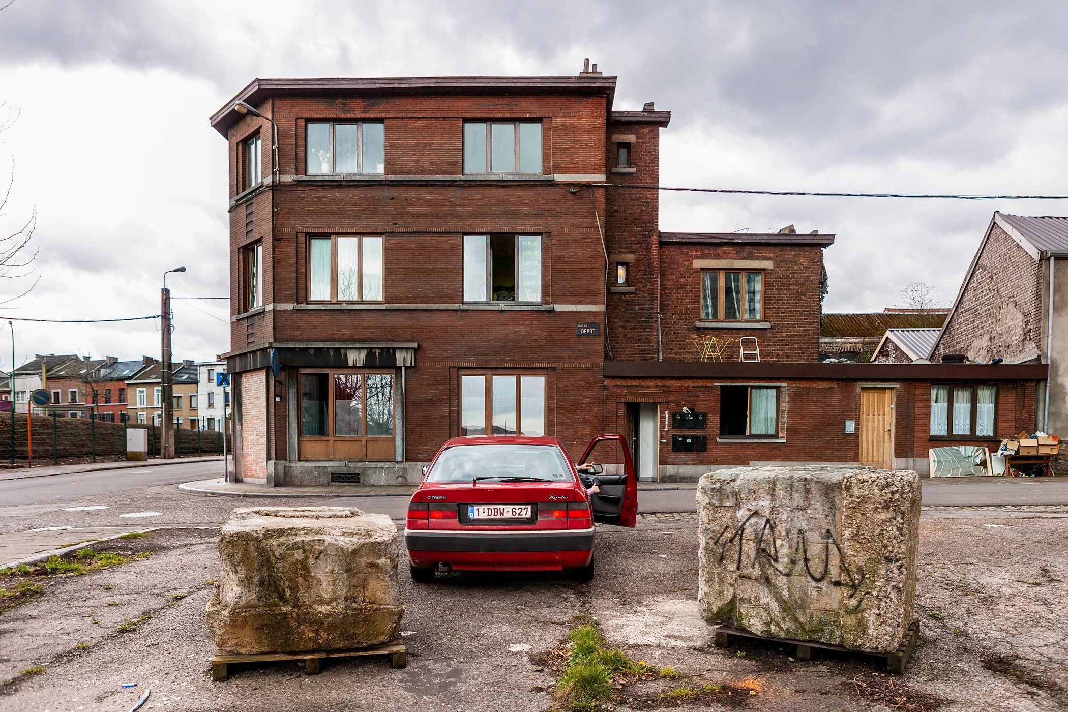 Een rode auto geparkeerd voor een bakstenen gebouw met meerdere verdiepingen en grote ramen op een straat in een stad.