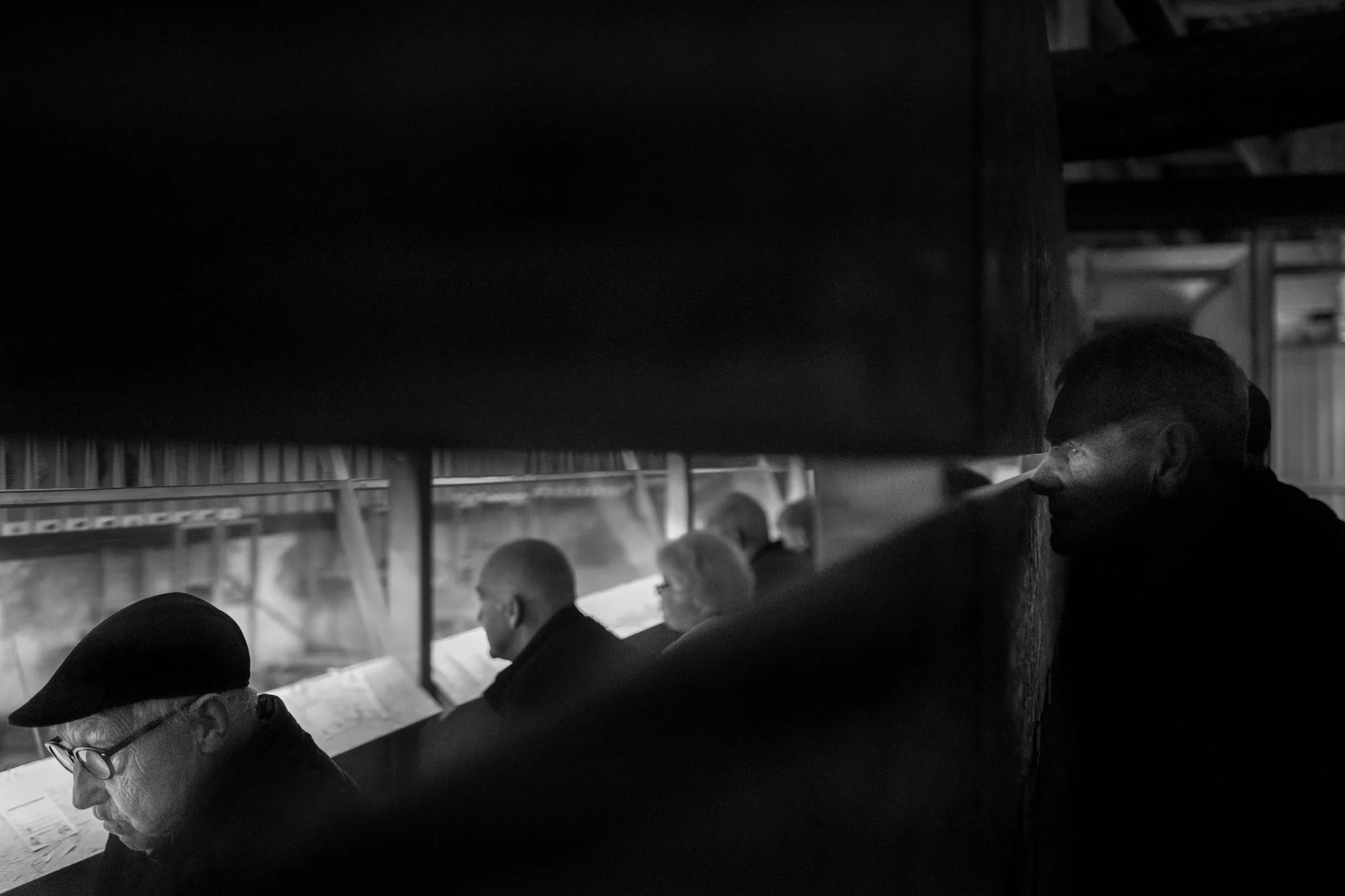 Zwart-wit foto van meerdere mensen die zitten en lezen, met een persoon op de voorgrond rechts die in de schaduw staat