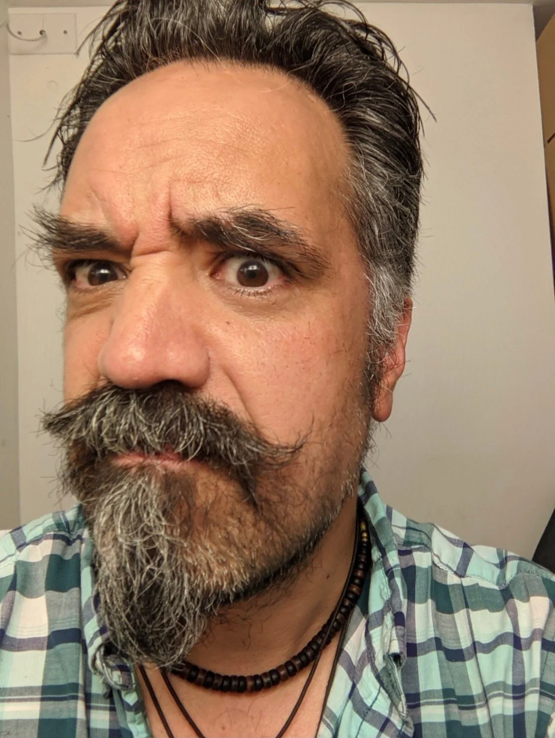 A close-up selfie of a middle-aged man with a crazy mustache and a wild look in his eyes.