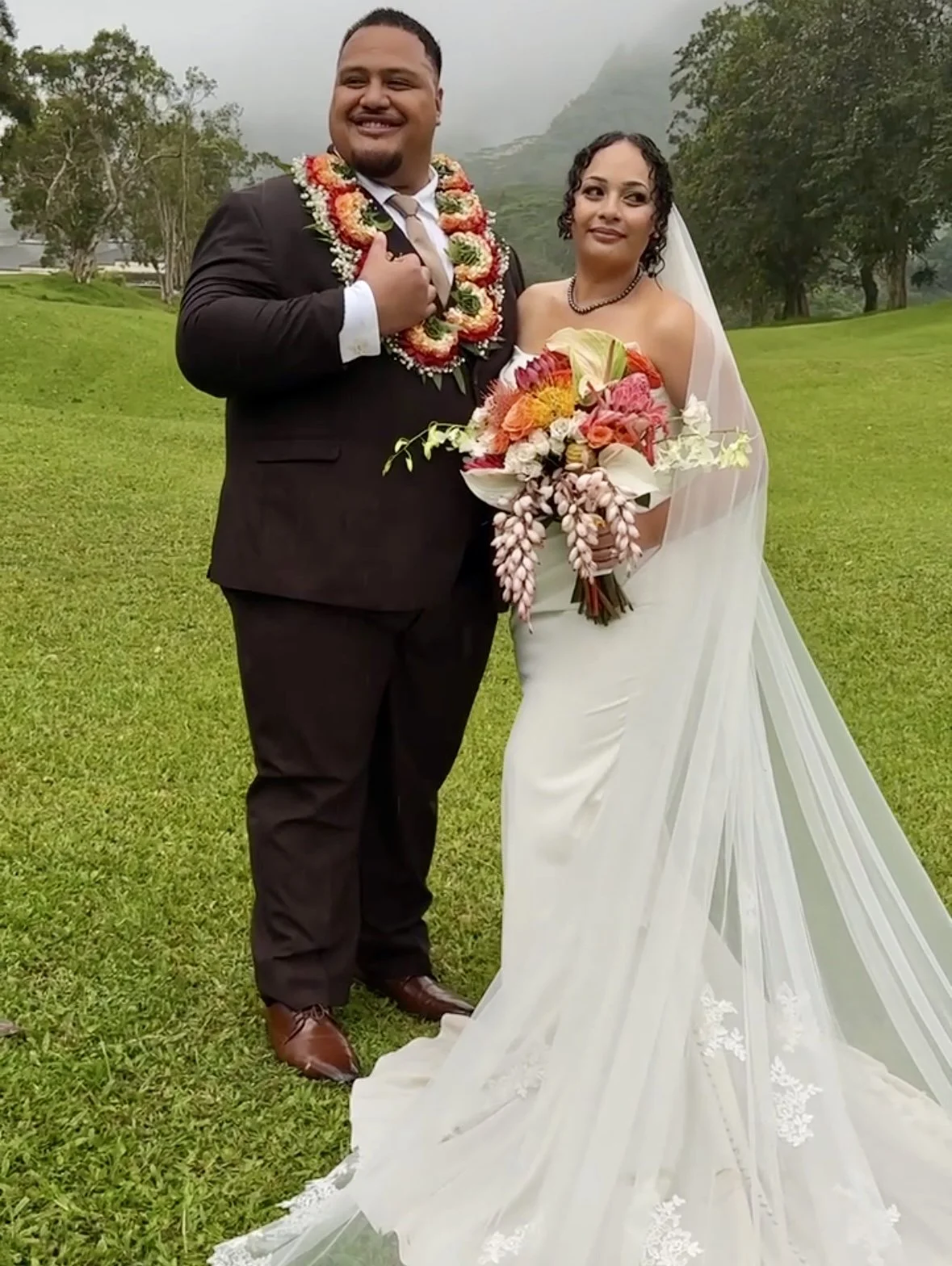 Bride and groom during couples portraits on Oahu with stunning floral bouquet and flowing veil