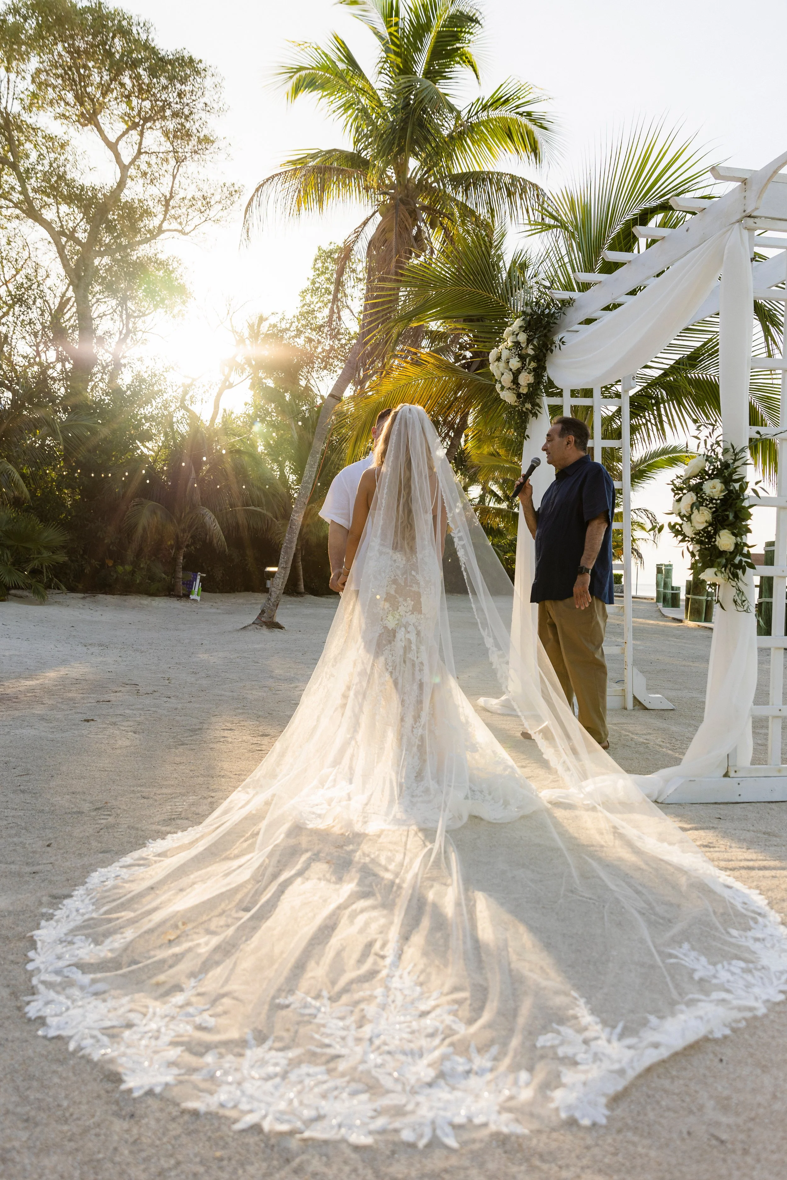 Bride and groom exchanging vows under a floral wedding arch at Key Largo Lighthouse Beach Resort