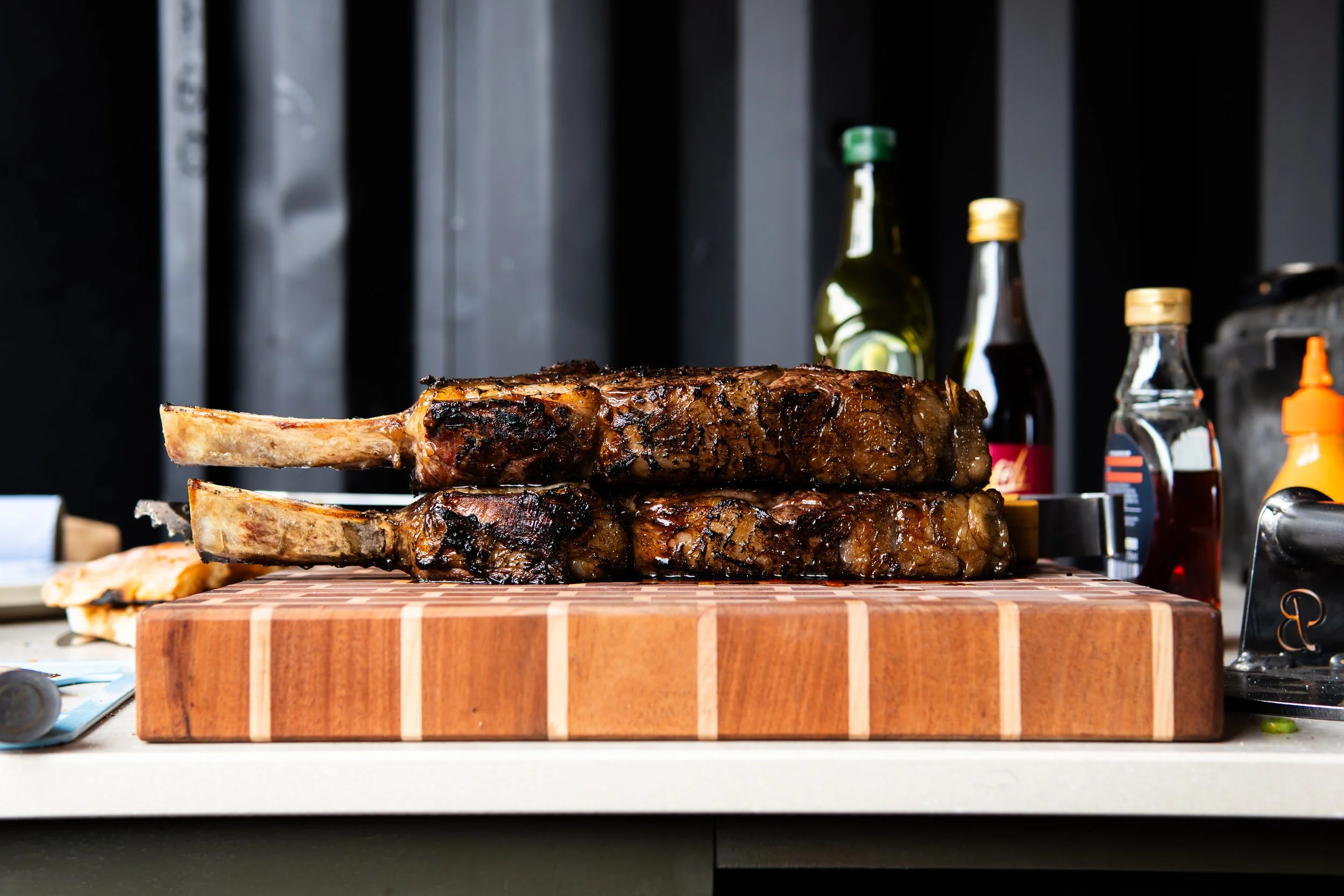 Two cooked racks of ribs on a wooden cutting board surrounded by condiments and sauces.