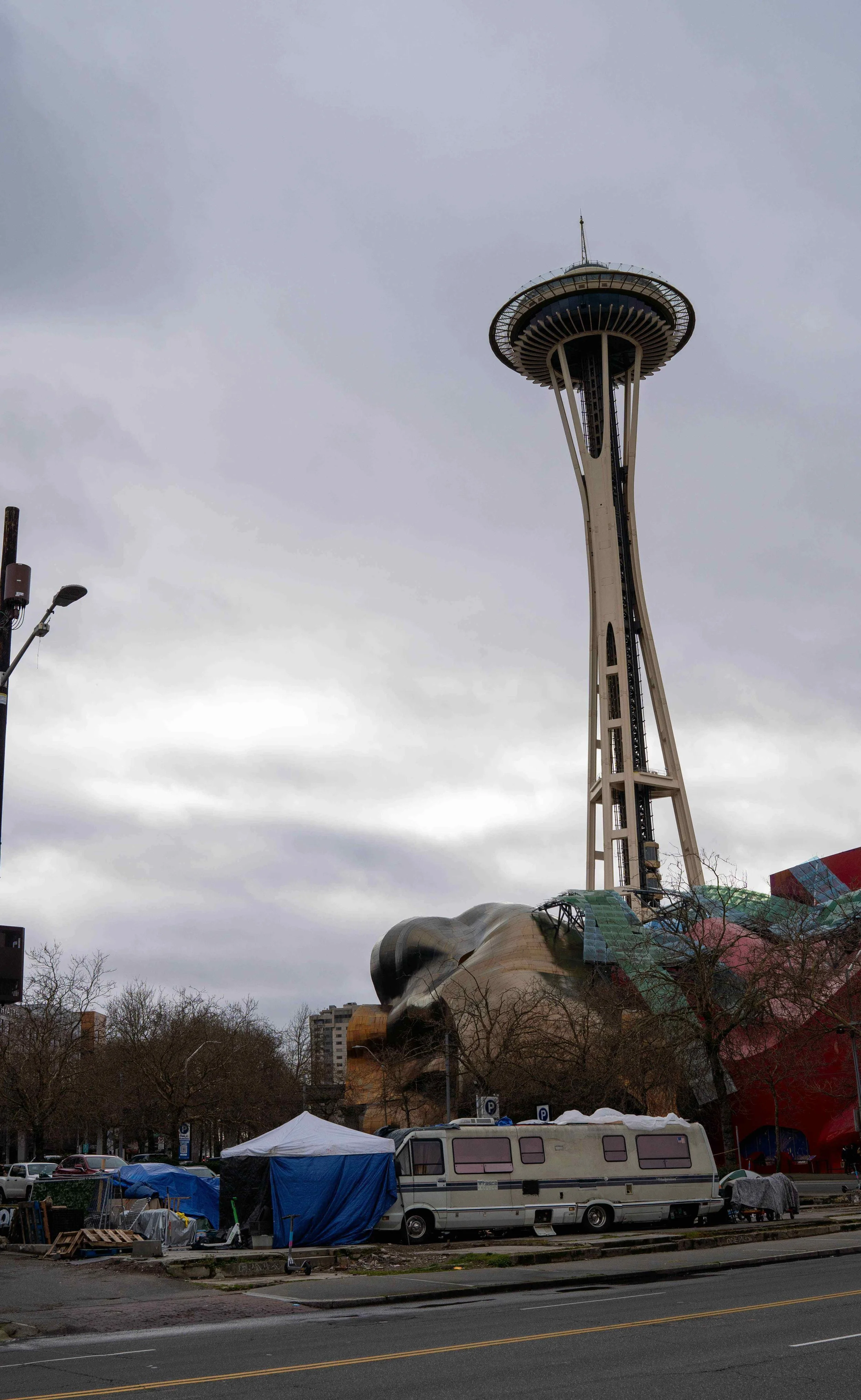 Iconic view of the Space Needle and MoPOP museum behind a parked RV and homeless tents at 5th Ave N and Harrison St, Seattle.