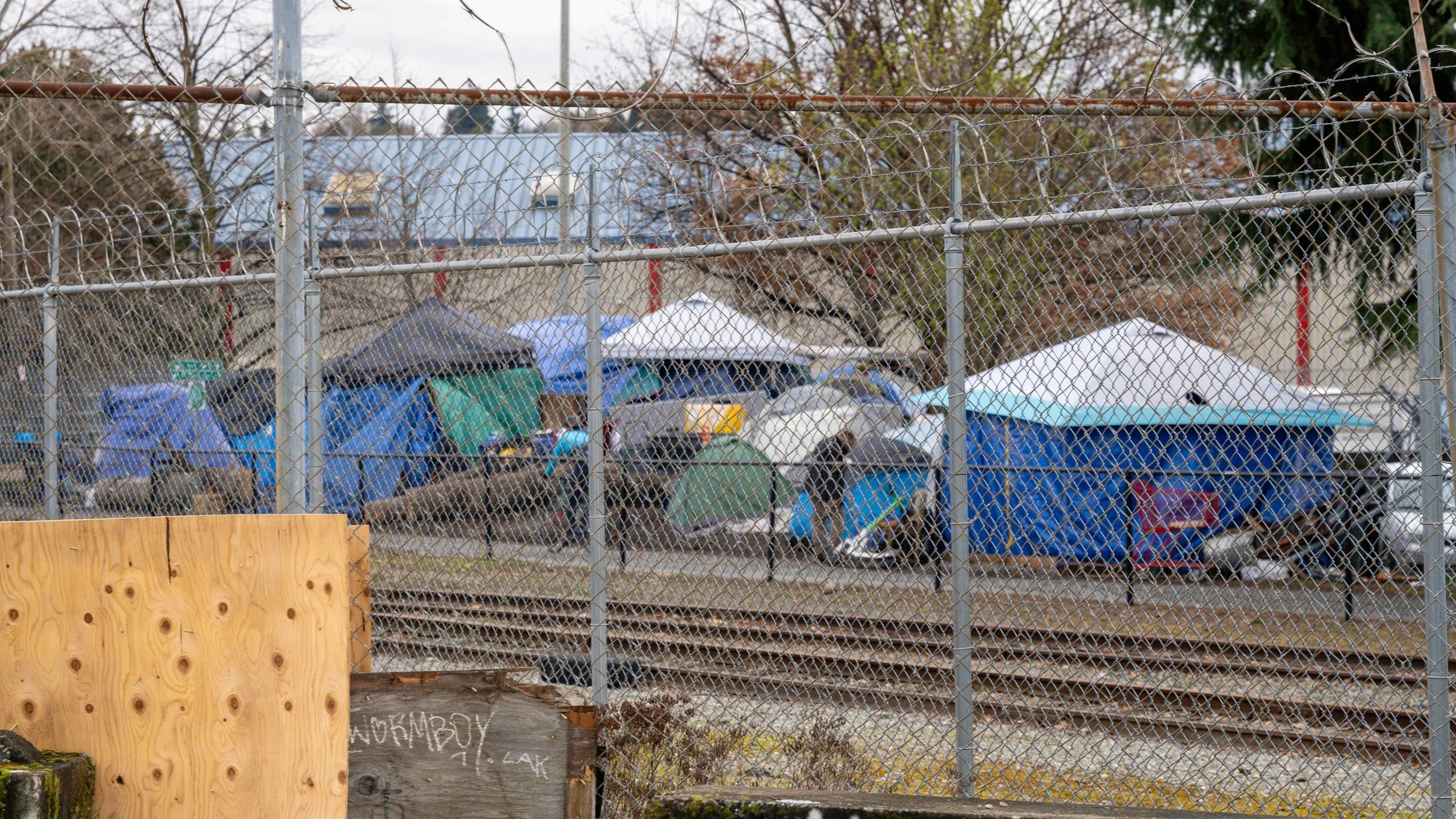 Wide view of a dense tent city with white canopies and blue tarps in the industrial Interbay corridor of Seattle.