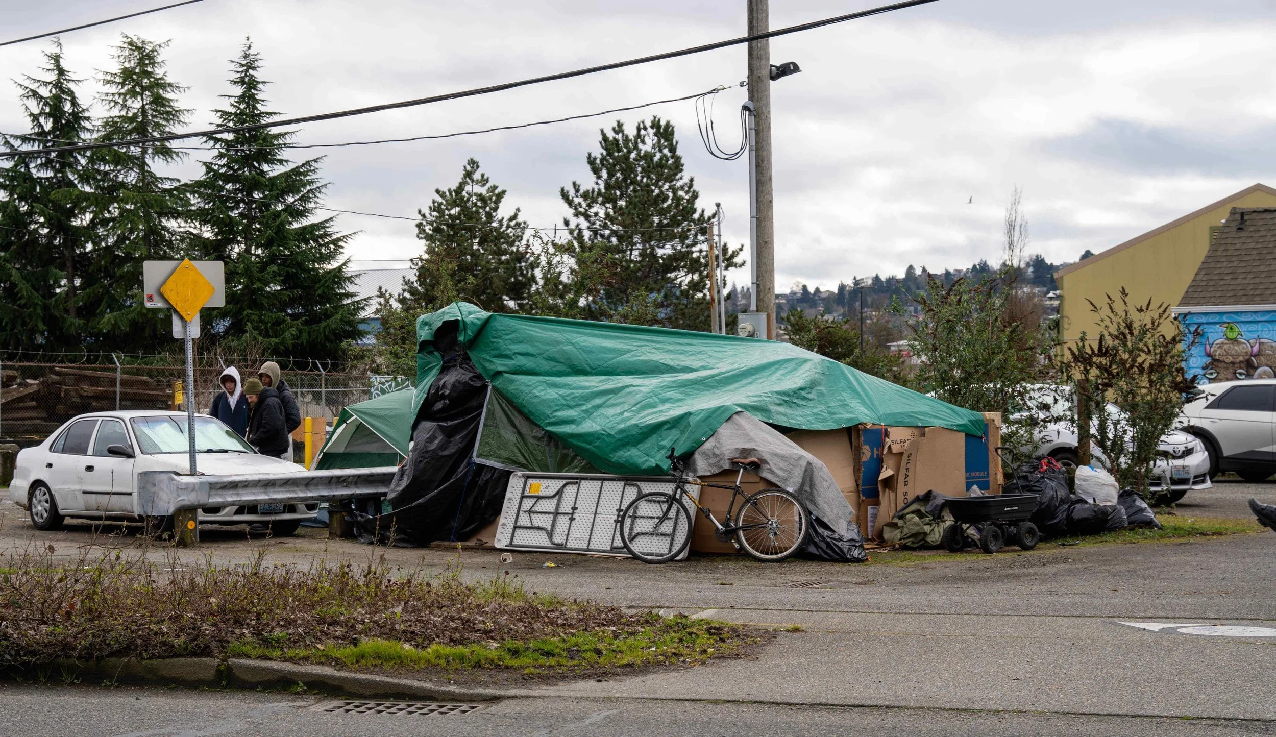 A large makeshift green tarp shelter and a white sedan parked near the BNSF railroad tracks in Interbay, Seattle.