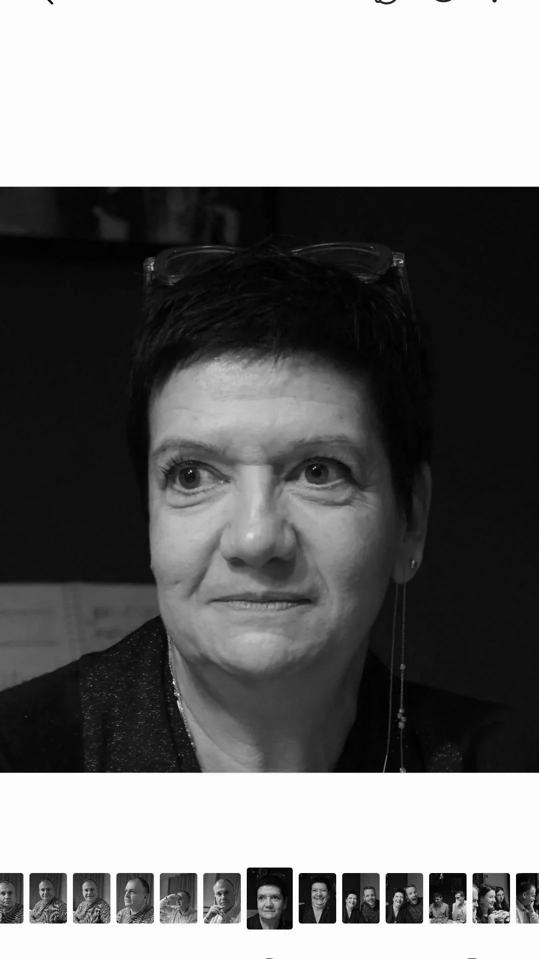 Une femme avec des cheveux courts, portant des lunettes sur la tête et une petite boucle d'oreille, regarde légèrement sur la gauche. Photo en noir et blanc.