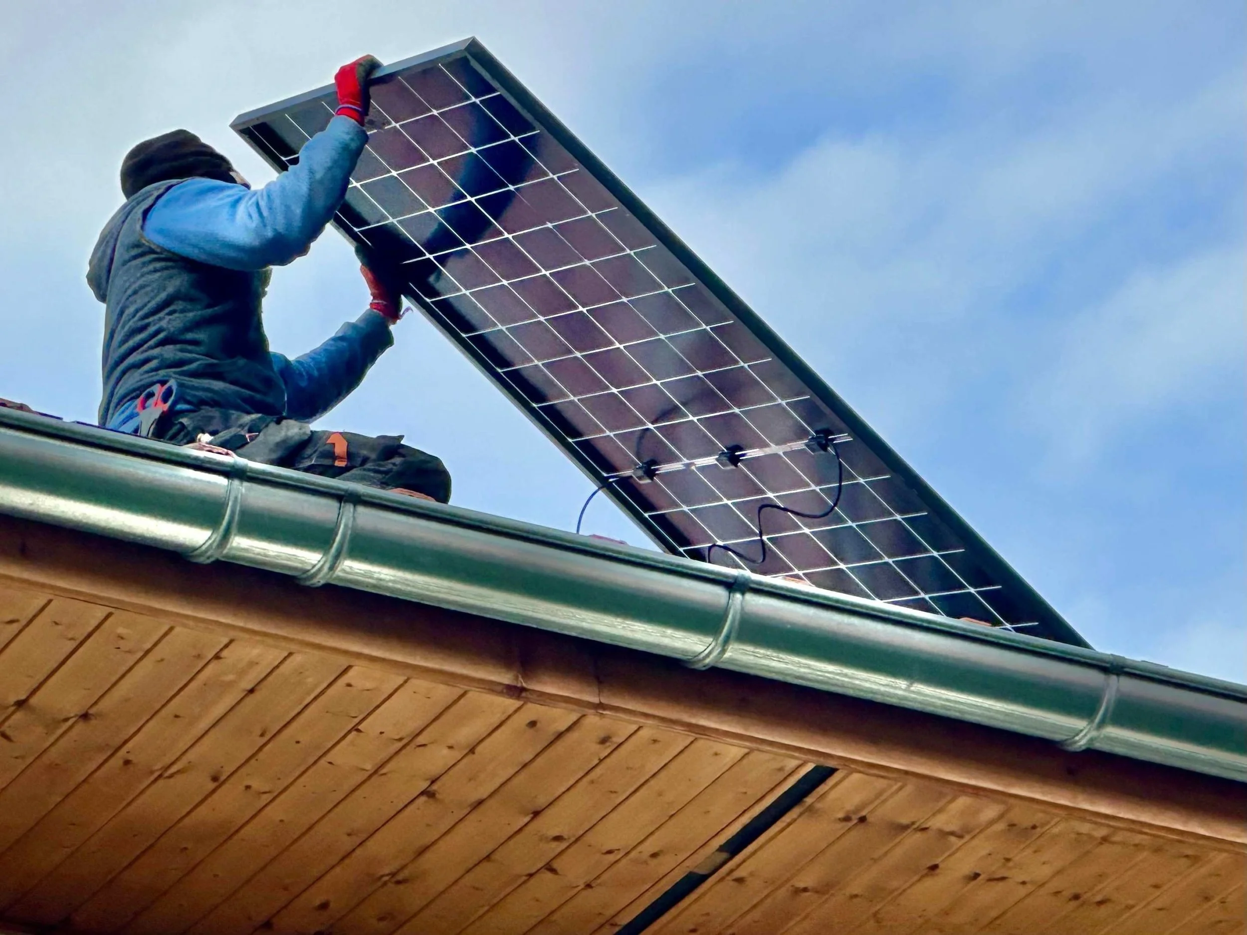 Un homme installe un panneau solaire sur le toit d'une maison.