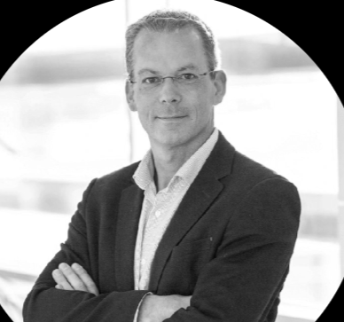 Portrait en noir et blanc d'un homme d'affaires portant un costume, avec bras croisés, dans un environnement professionnel.