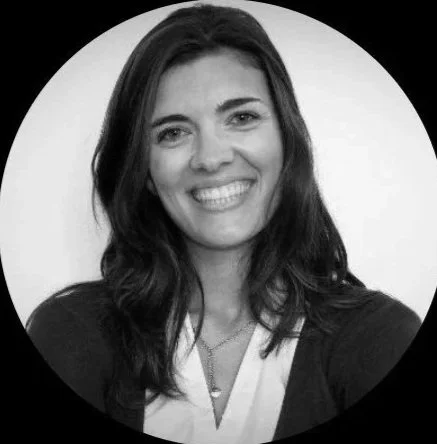 Une femme souriante avec des cheveux longs et foncés, portant un haut noir et un collier, dans un cercle blanc sur fond noir.