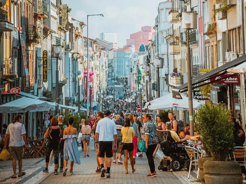Rue animée avec des passants, cafés en plein air, bâtiments colorés et boutiques, ambiance urbaine.