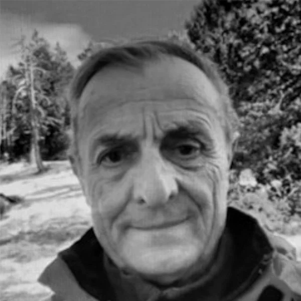 Un homme âgé prends une selfie en extérieur, avec des arbres en arrière-plan.