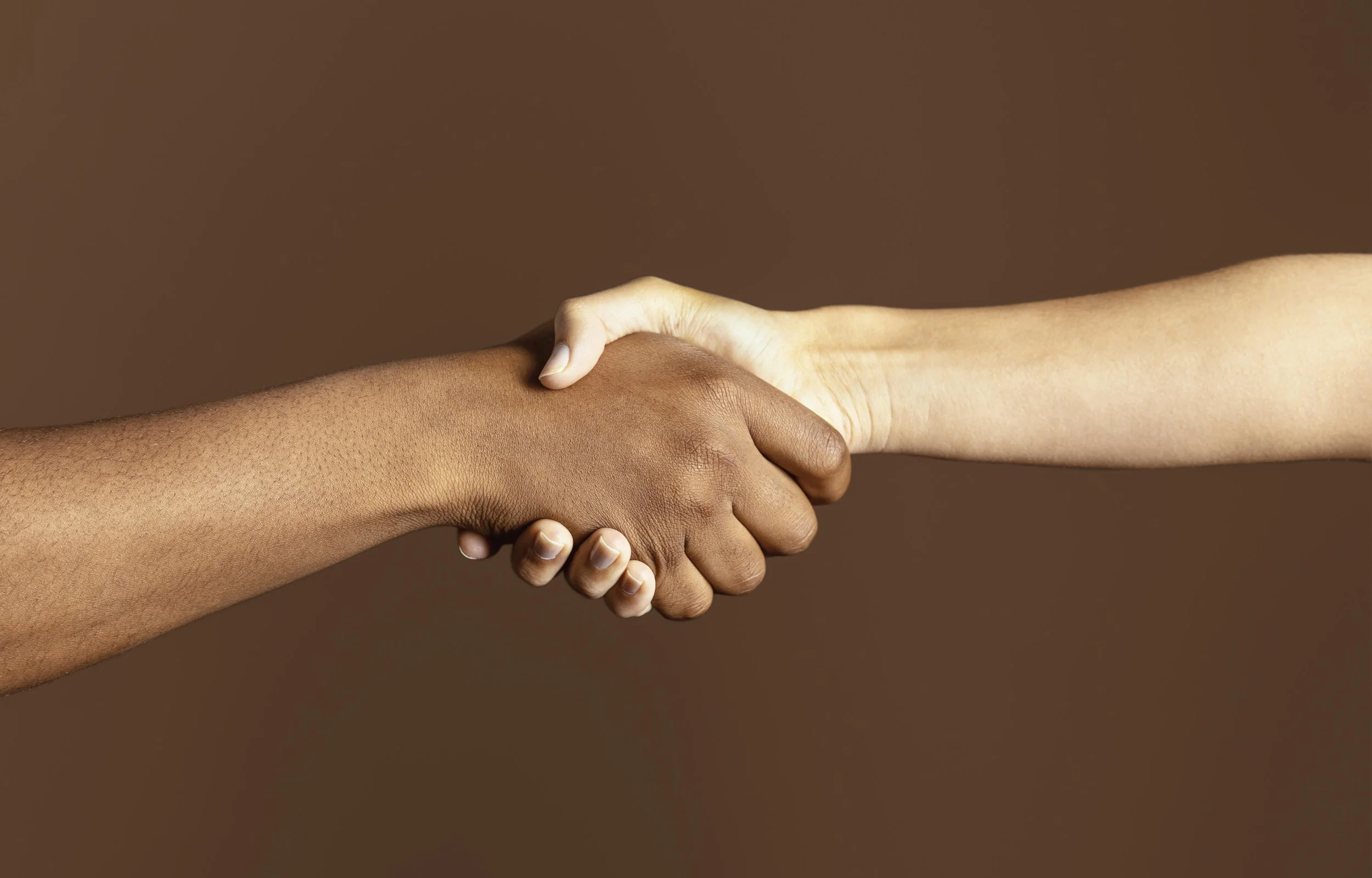 Deux mains qui se serrent la main, une de couleur de peau foncée, l'autre de couleur claire, contre un fond marron.