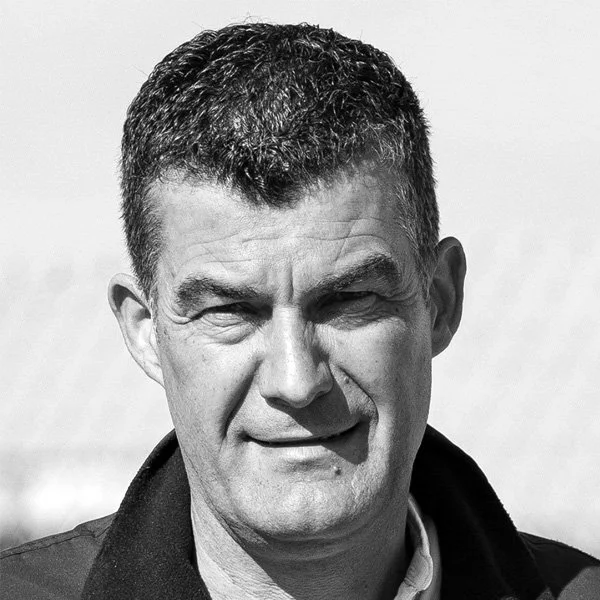 Portrait d'un homme avec des cheveux courts et foncés, portant une veste sombre, regardant vers l'objectif, en noir et blanc.