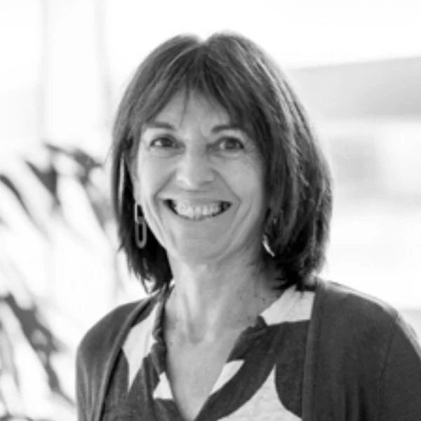 Une femme souriante avec des cheveux bruns et courts, portant une veste sombre et un haut à motifs, dans un environnement lumineux