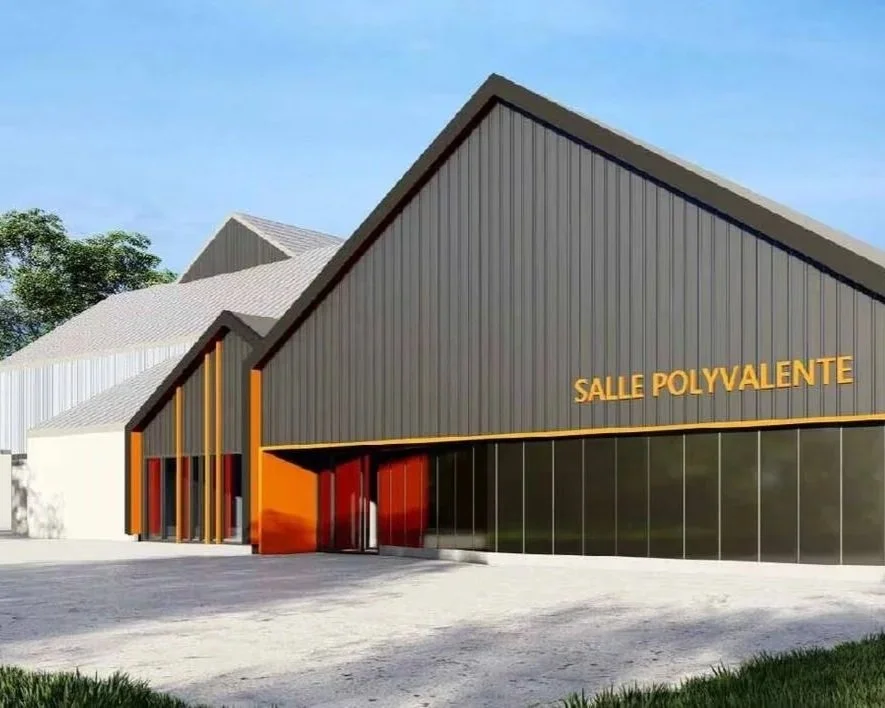 Bâtiment moderne avec des formes angulaires, façade en panneaux métalliques gris et orange, et lettres 'SALLE POLYVALENTE' en jaune.
