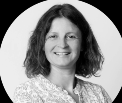 Portrait en noir et blanc d'une femme souriante avec des cheveux bouclés, portant une blouse claire.