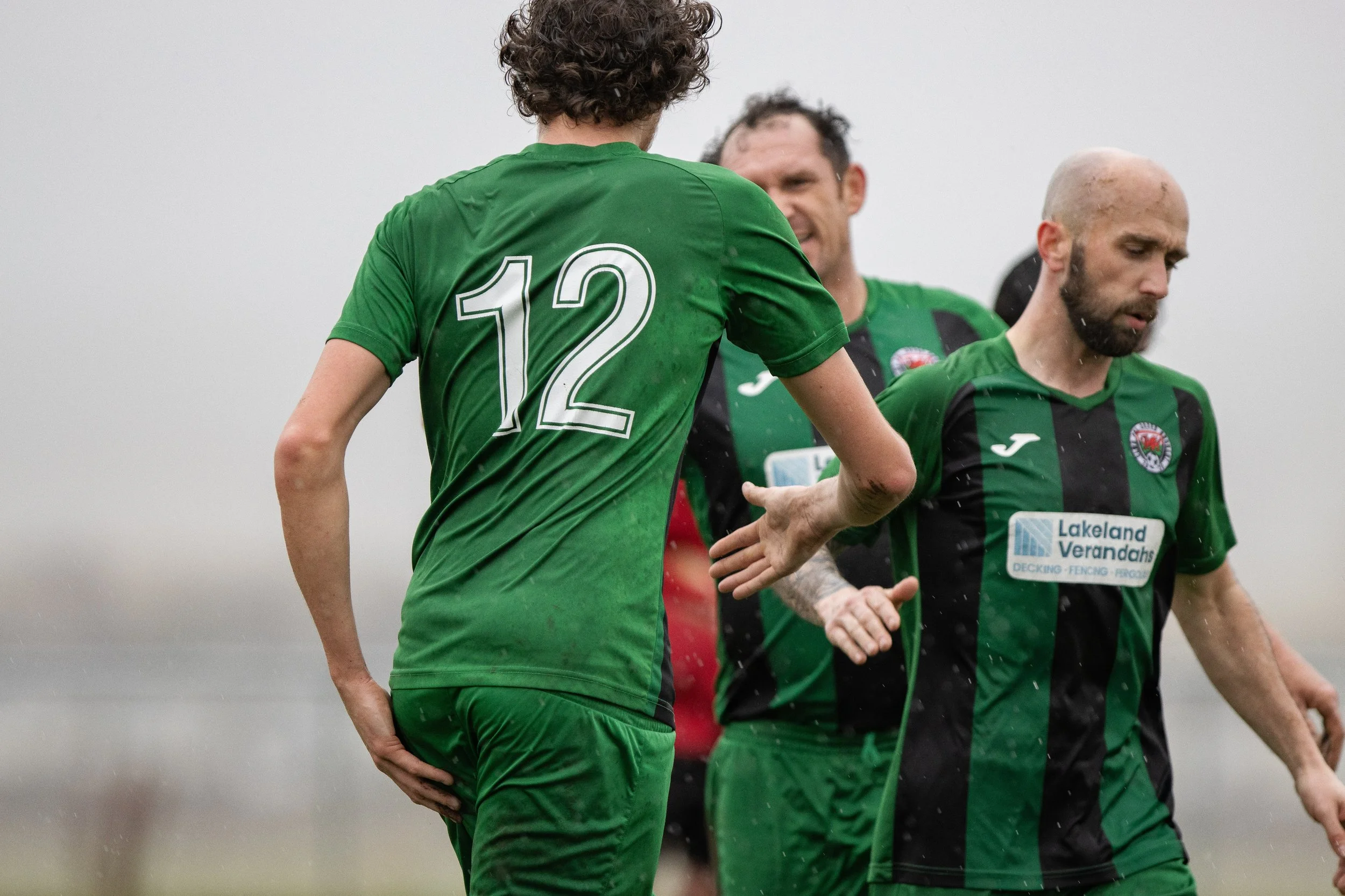 Soccer players wearing green jerseys on a rainy day, celebrating during a match.