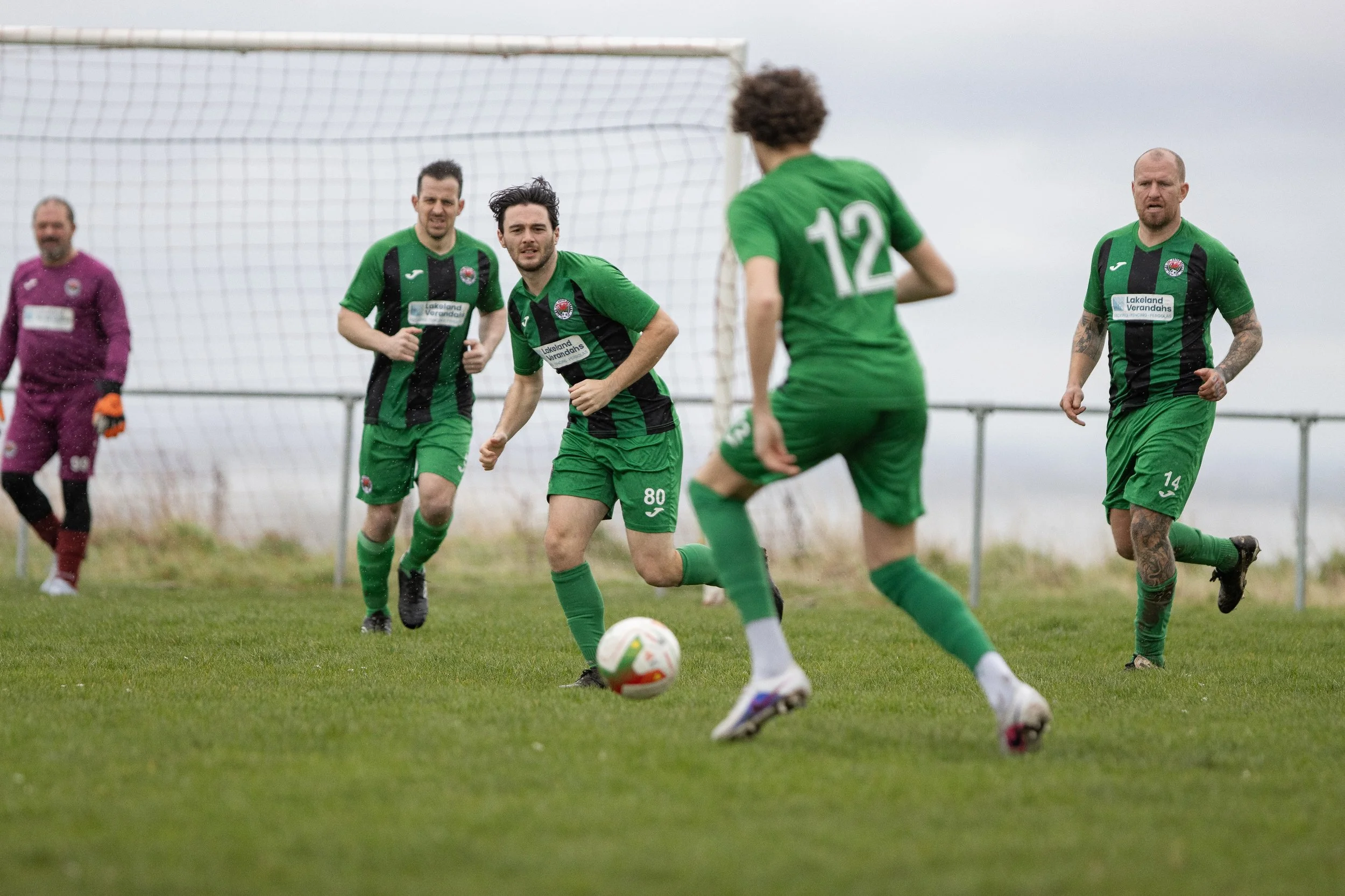 Soccer players in green uniforms playing on a grassy field with a goal in the background.