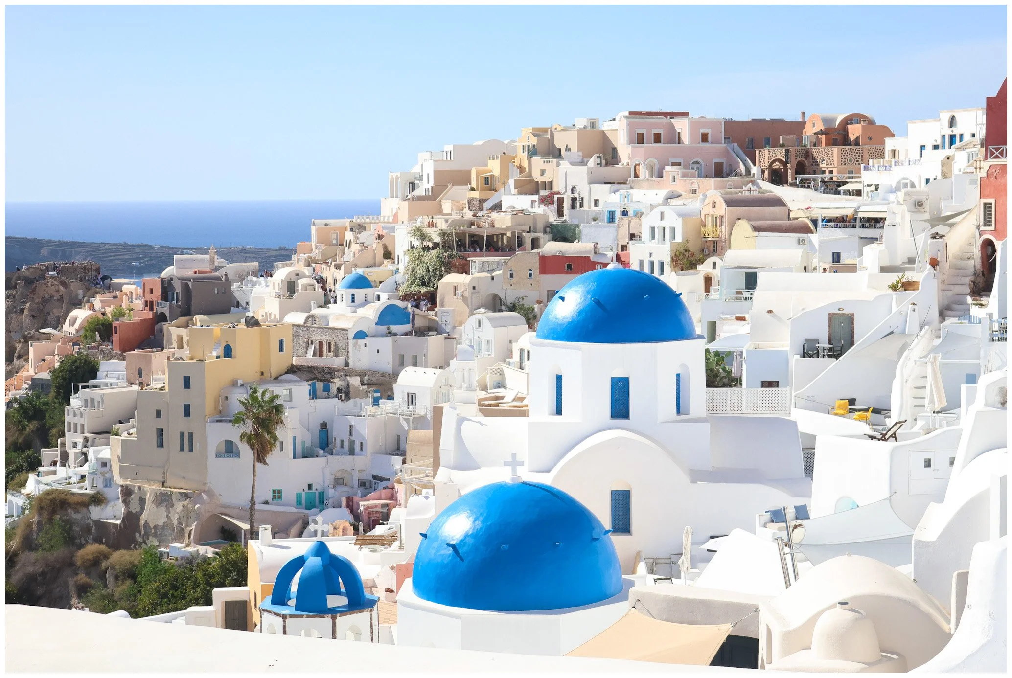 White buildings with blue domes on a hillside in Santorini, Greece, overlooking the sea.