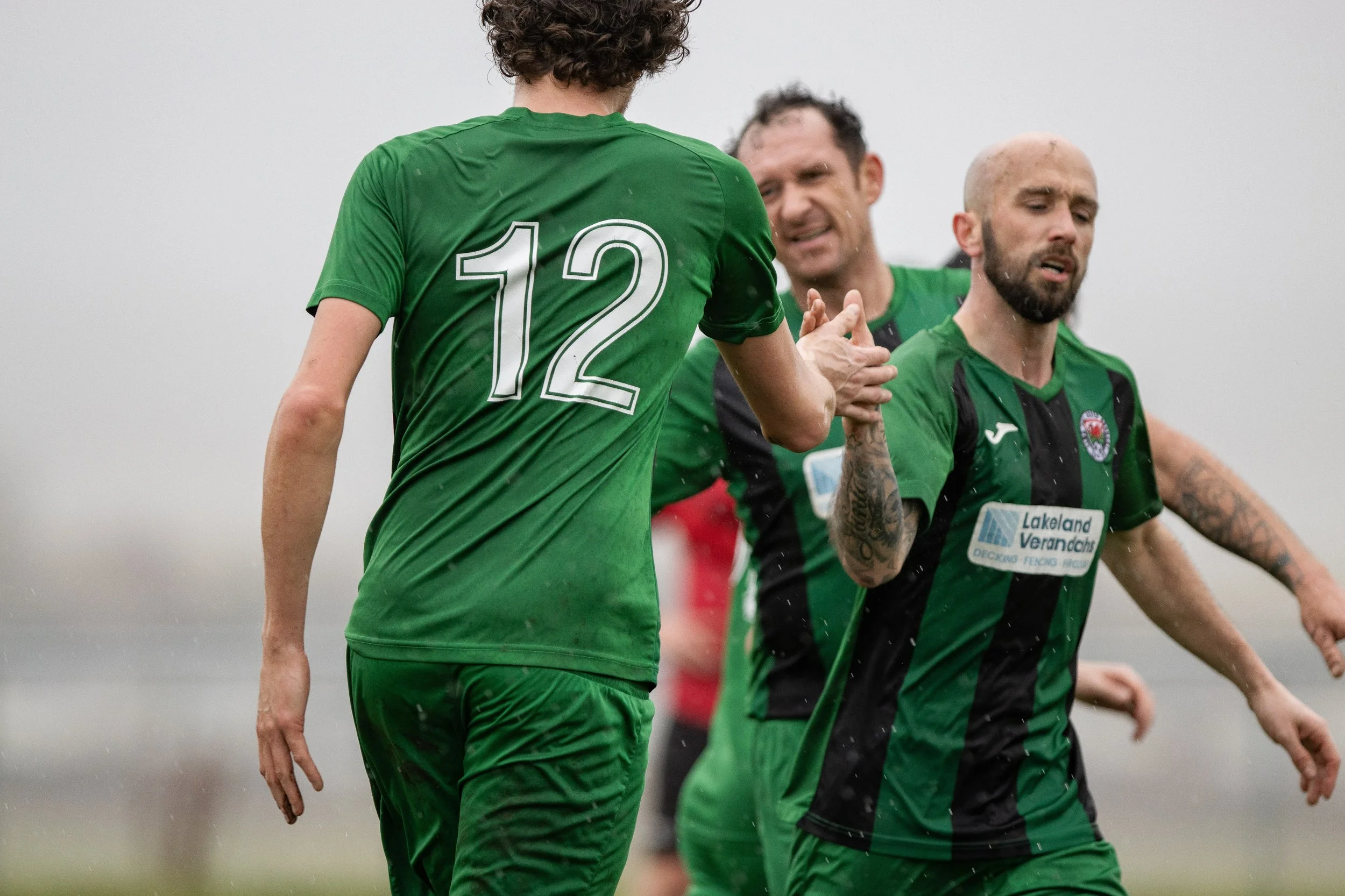 Soccer players in green jerseys celebrating on the field, with some water droplets visible.