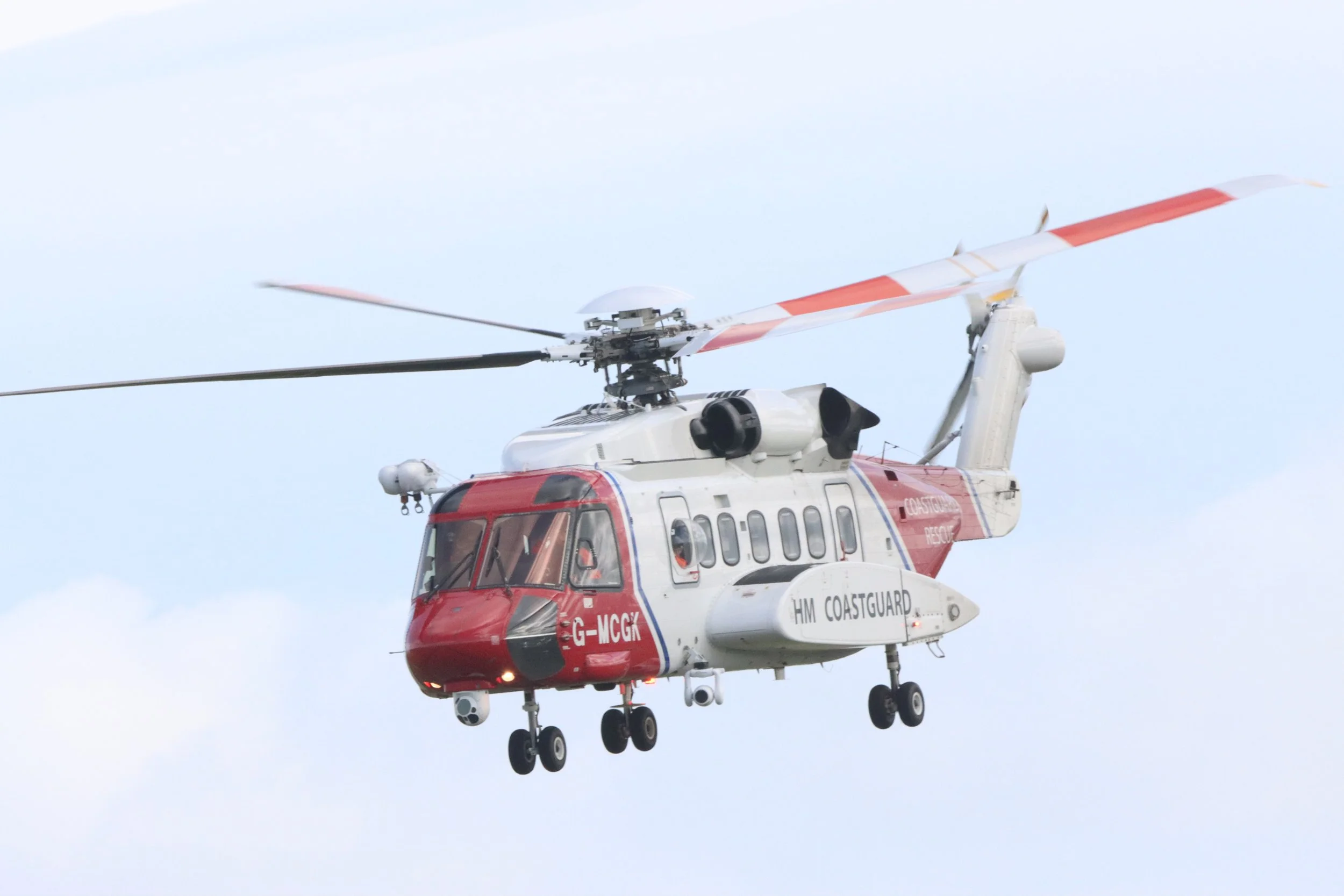 A helicopter flying in the sky with white and red markings and the words 'HM COASTGUARD' on the side.