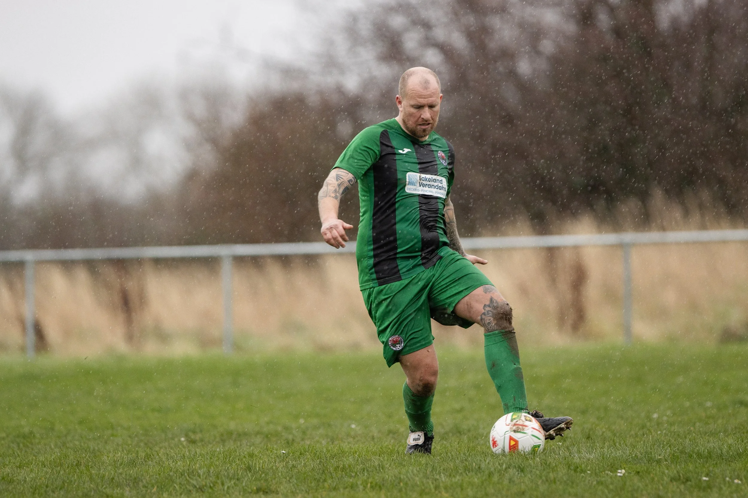 A man wearing a green and black soccer uniform playing soccer on a wet field.