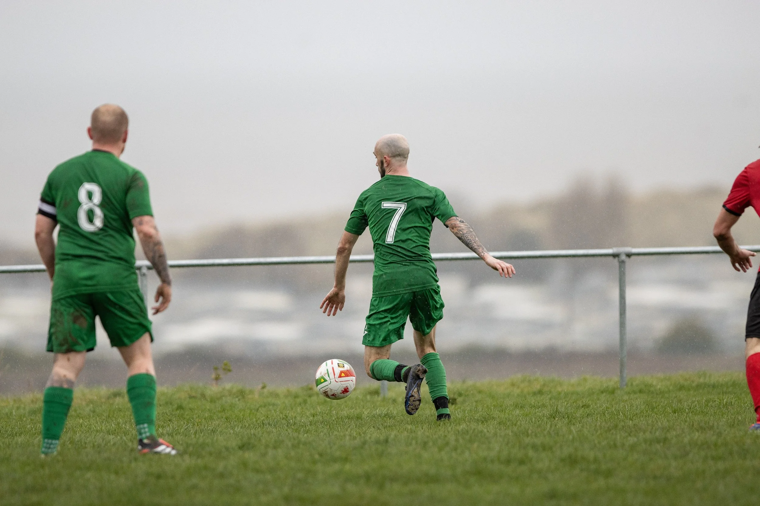 Soccer players in green uniforms playing on a field on a rainy day