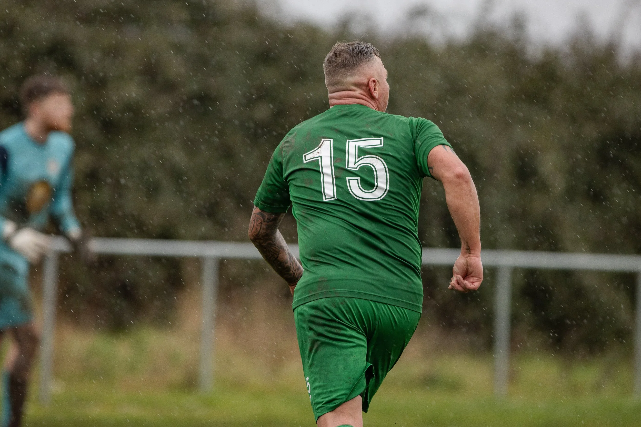 A soccer player wearing a green jersey with the number 15, running on a field in rainy weather.