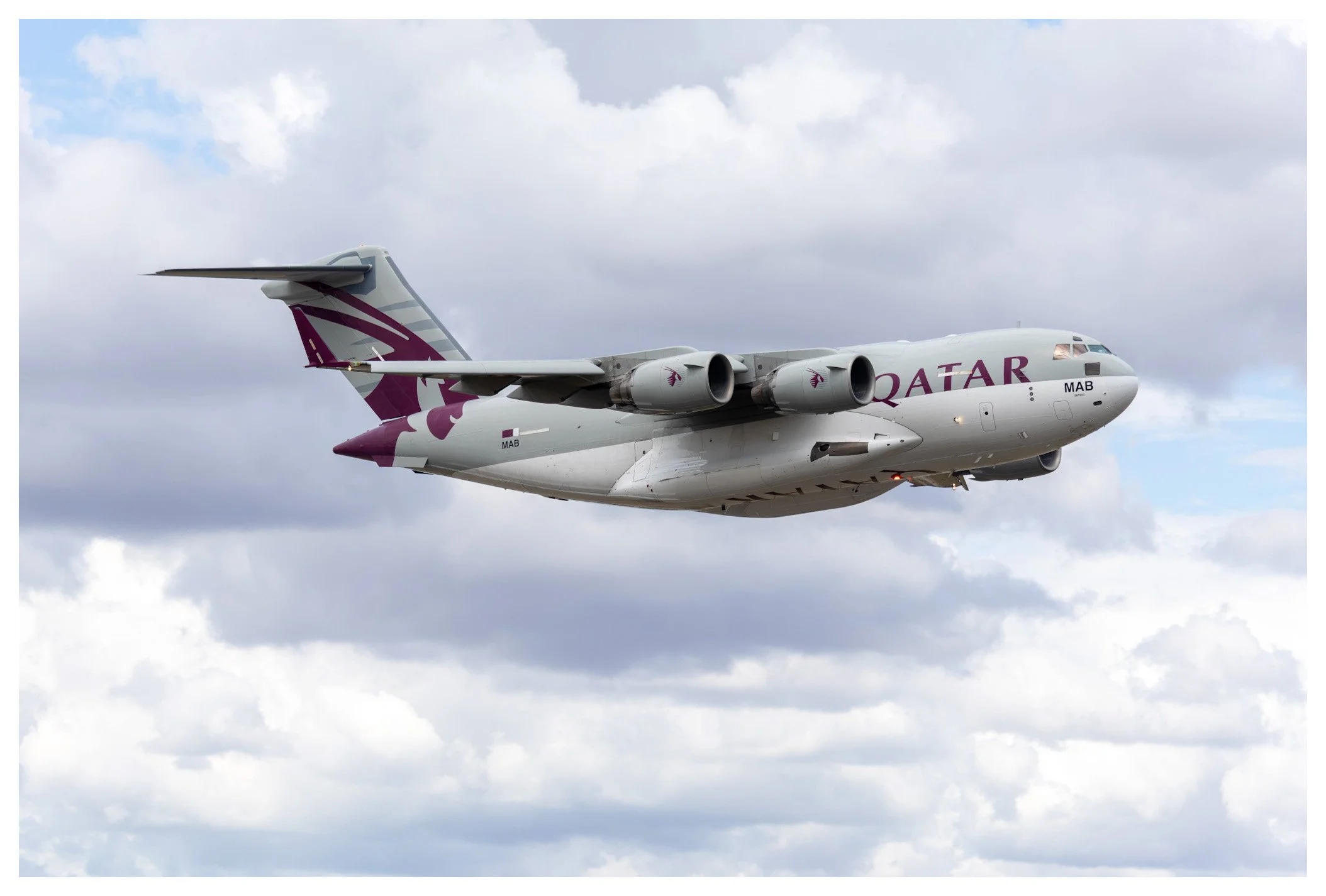 A Qatar Airways cargo airplane flying through a partly cloudy sky.