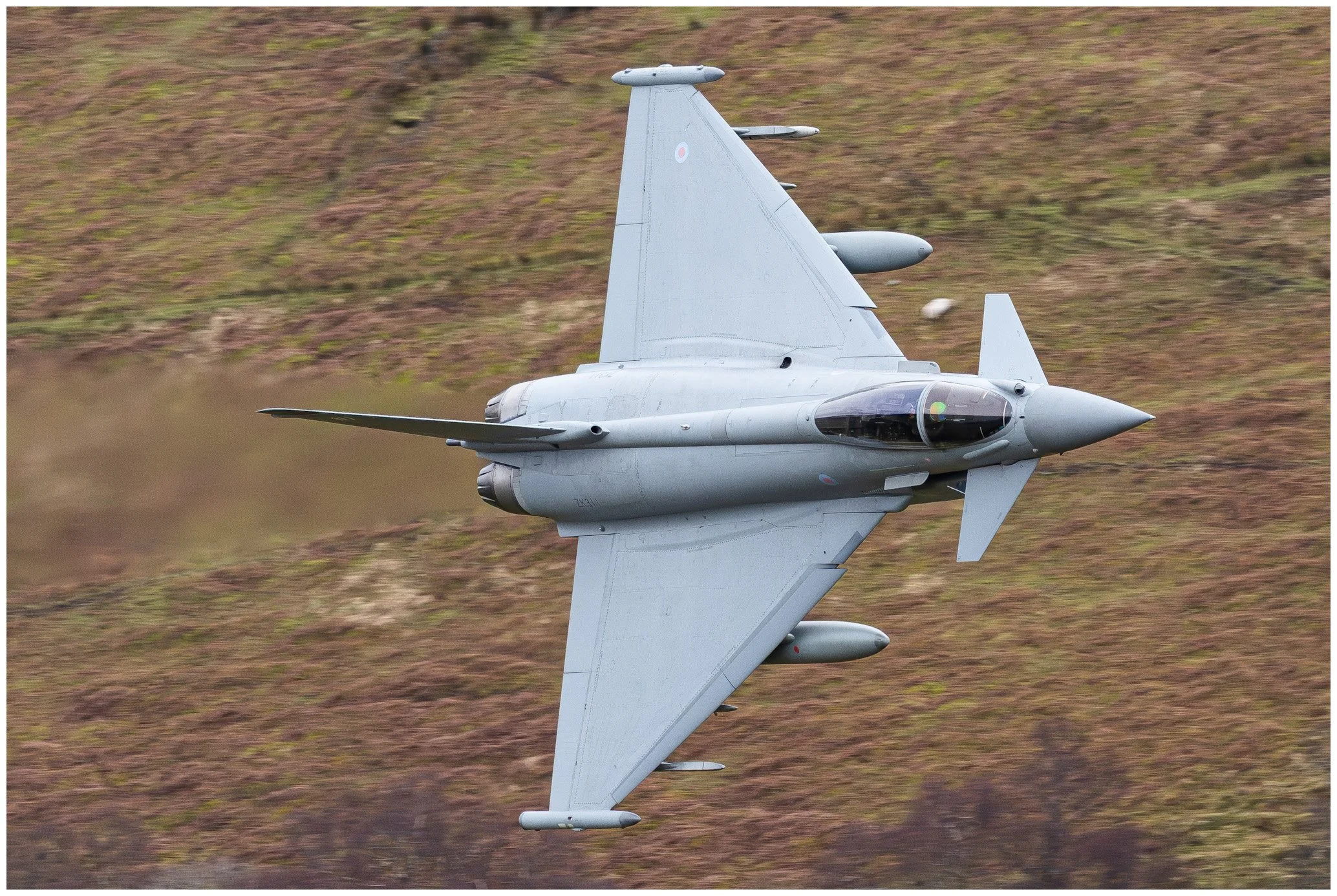 A military fighter jet flying low over hilly terrain.