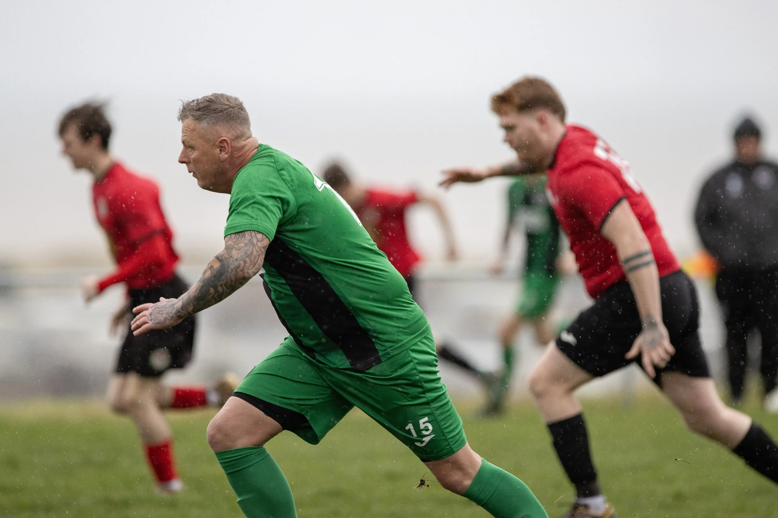 A group of rugby players in red and green jerseys running on a field in rainy weather.