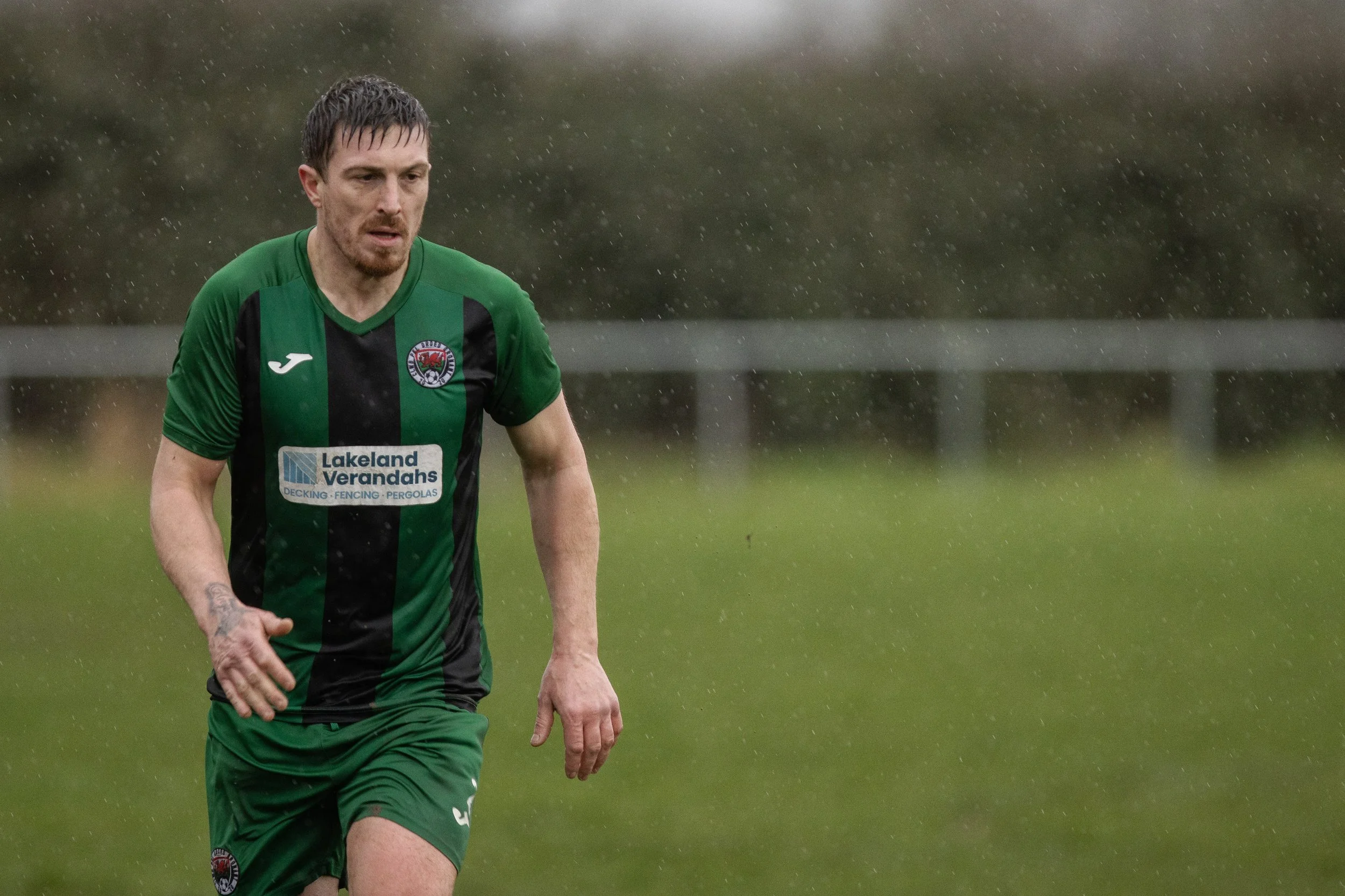 A male soccer player in a green and black uniform running in the rain on a soccer field.