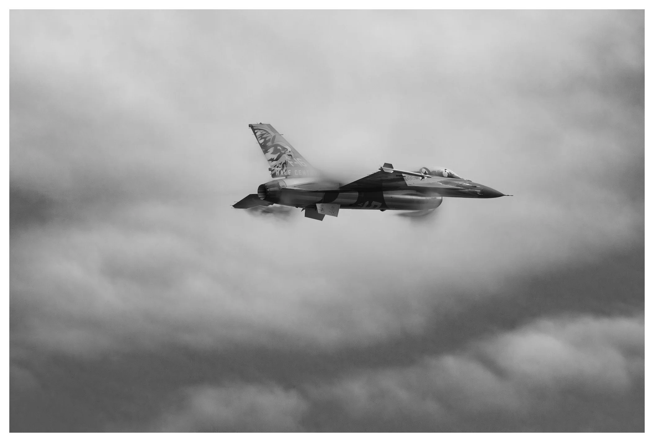 A fighter jet flying through cloudy skies, leaving a vapor trail behind.