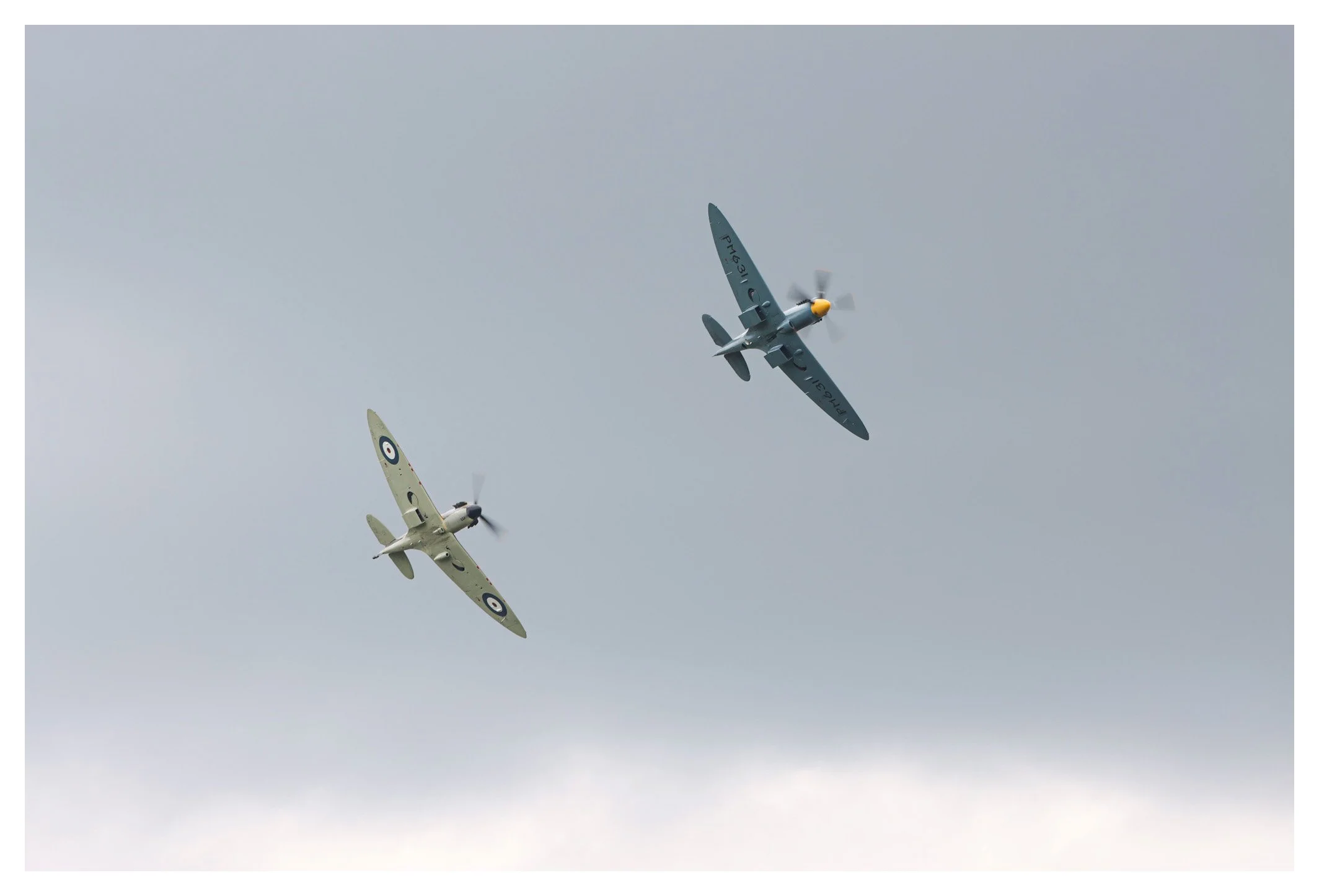 Two vintage fighter planes flying in formation against a cloudy sky.