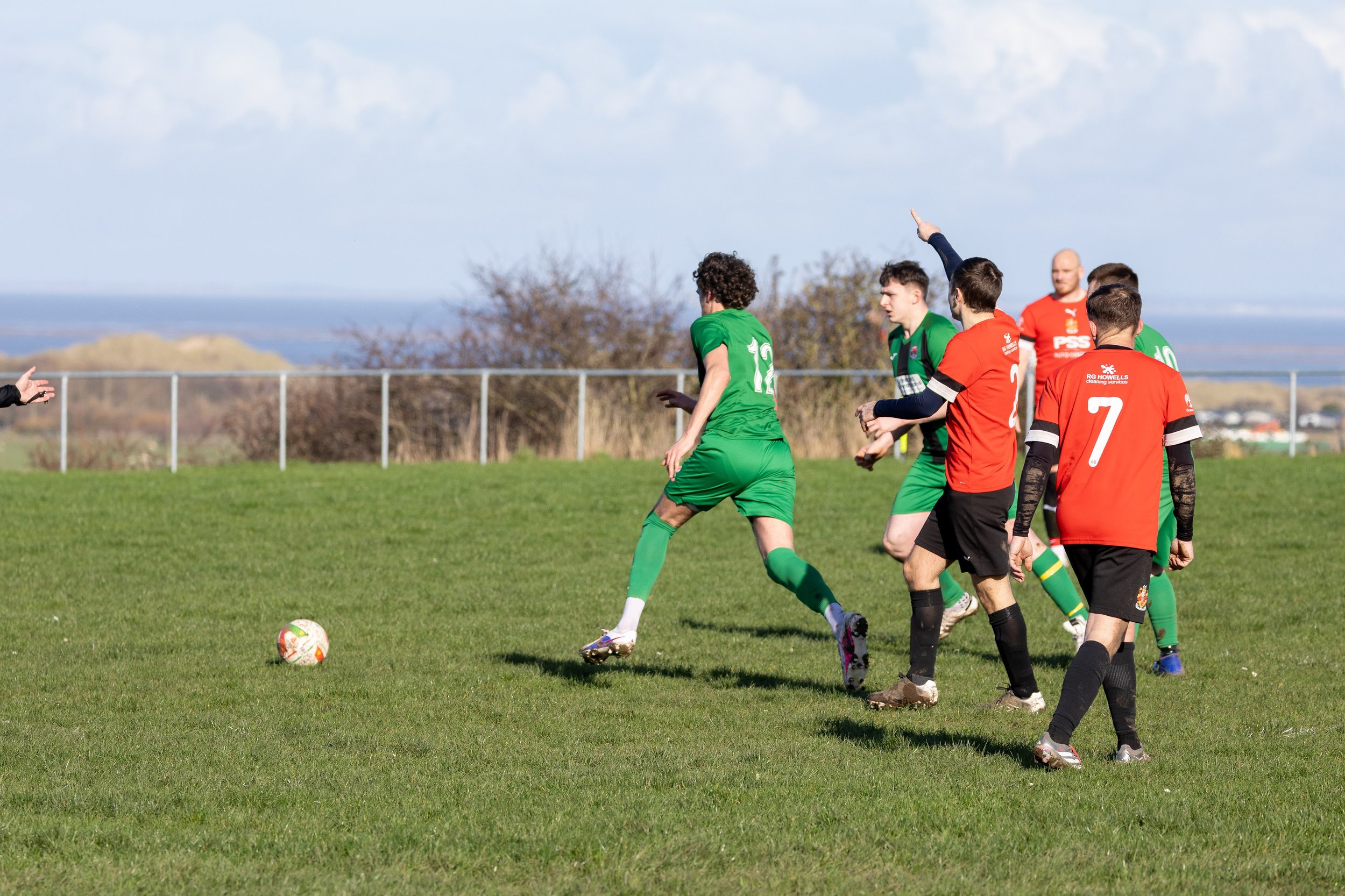 Soccer players in green and red jerseys on a grassy field during a game.
