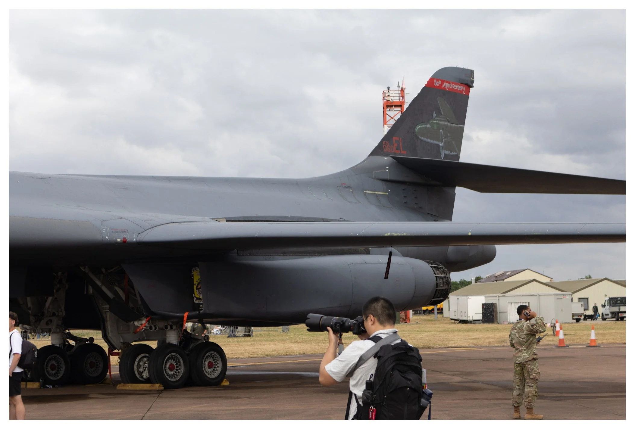 A military aircraft on display at an airfield, with people observing and taking photographs, under a cloudy sky.