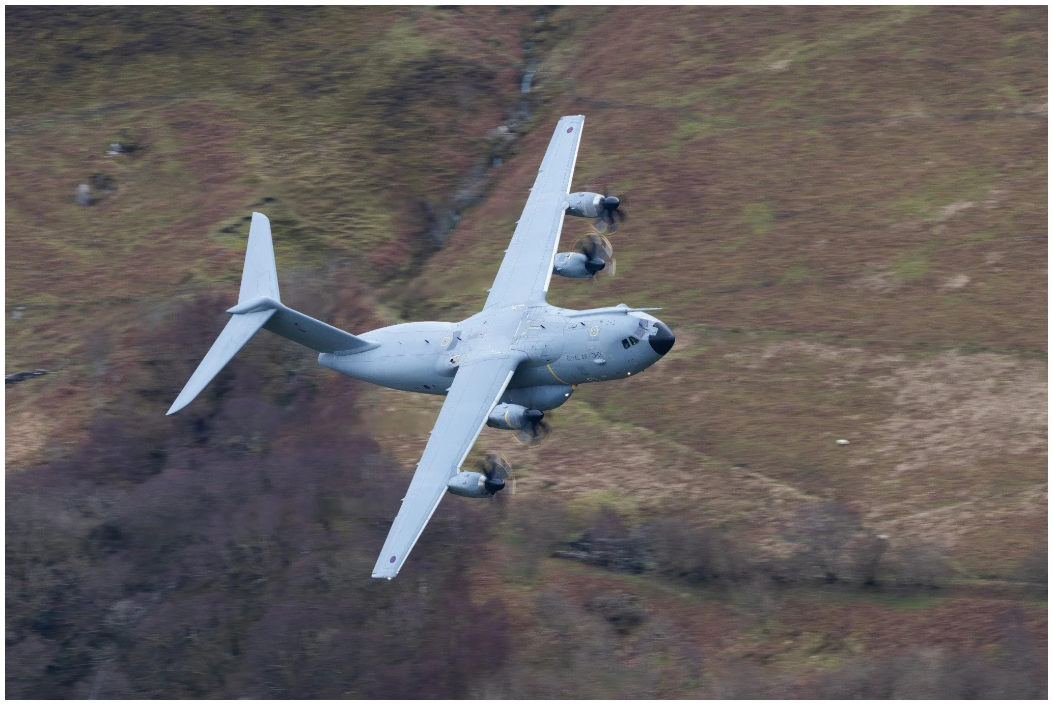 A military aircraft flying low over a hilly terrain with patches of grass and small bushes.