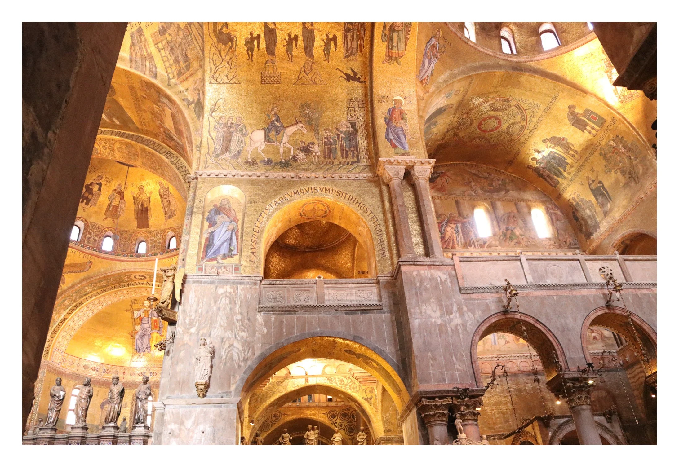 Interior of a church or cathedral with gold mosaics on the ceiling depicting religious figures and scenes, and statues along the lower walls.