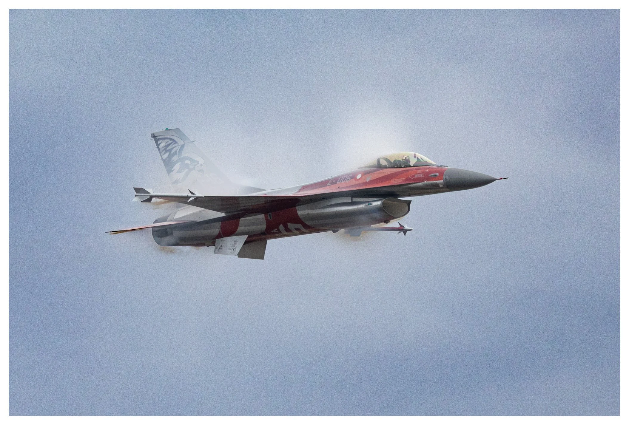A fighter jet flying through a cloudy sky with vapor trails.