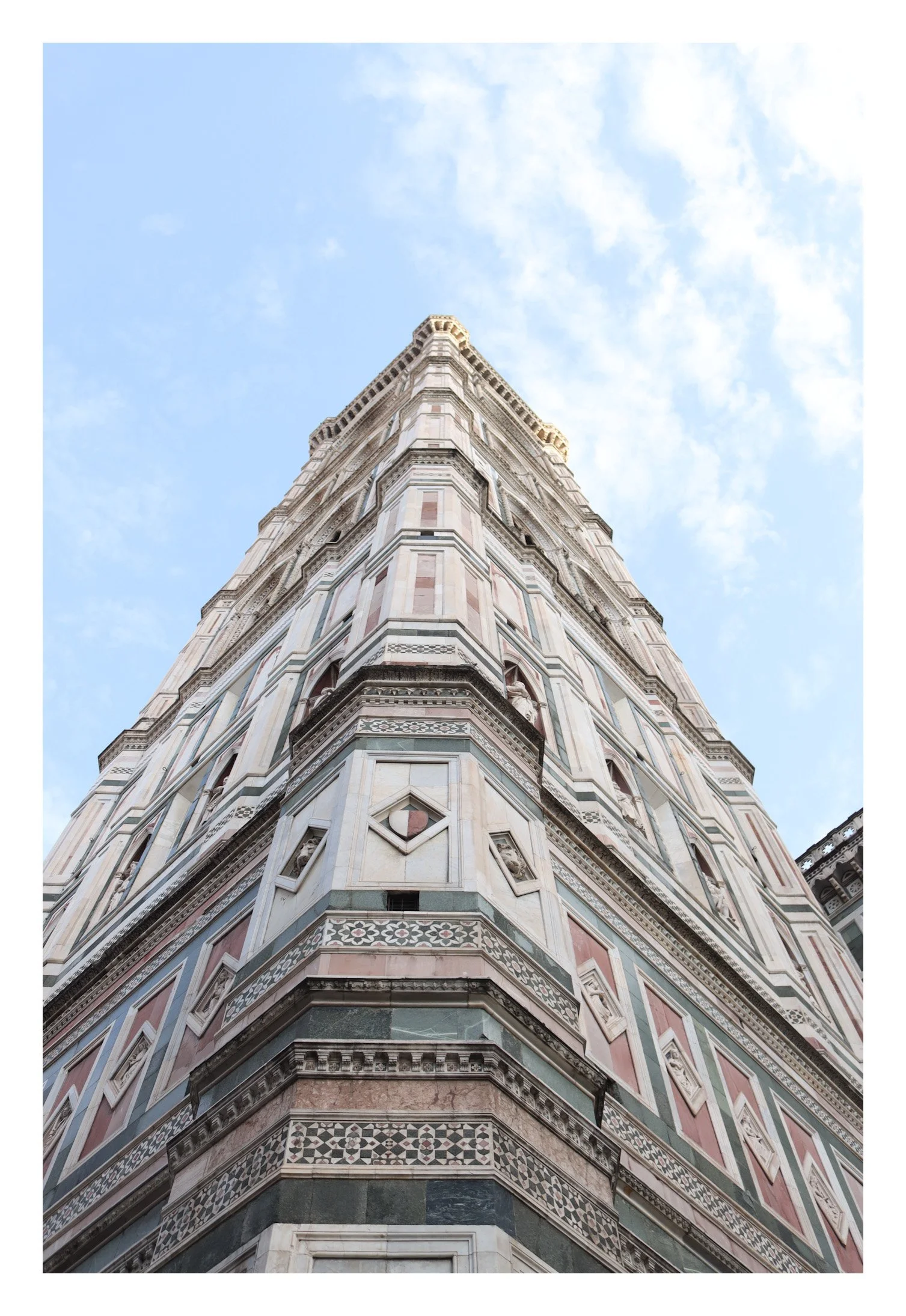 Low-angle view of the Leaning Tower of Pisa against a blue sky with some clouds.