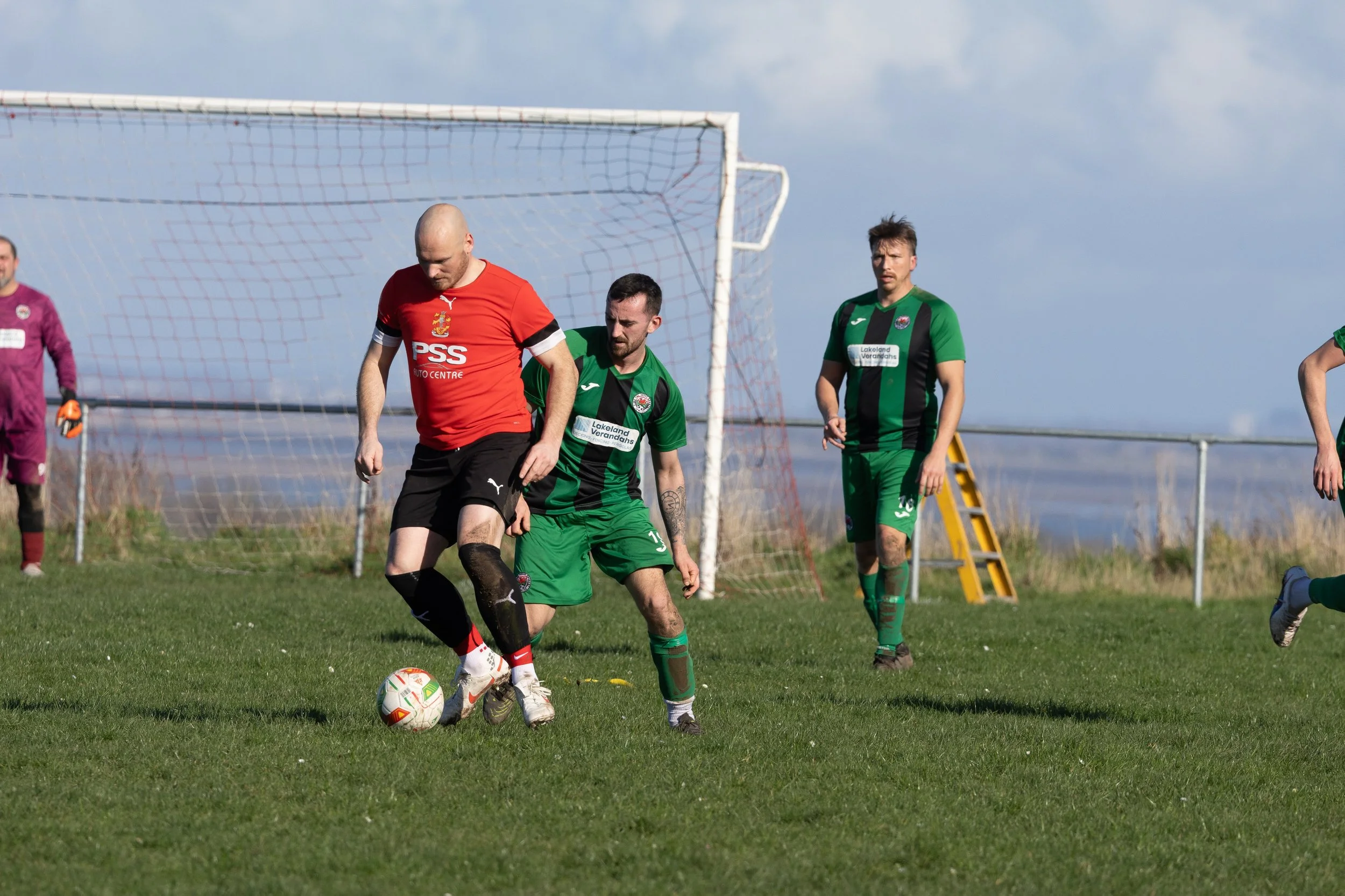 Soccer players competing for the ball on the field during a match with a goalpost and net in background.