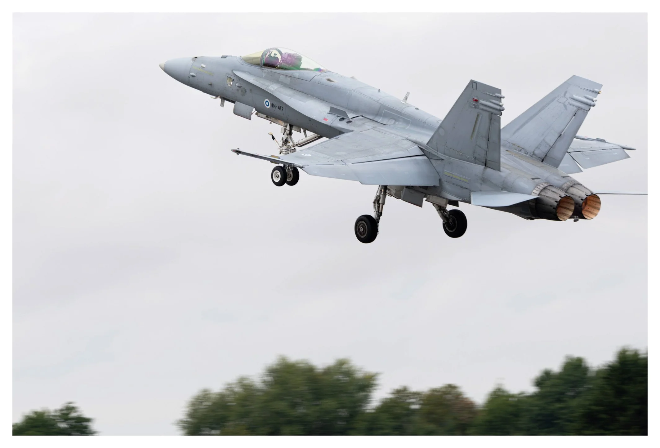 A fighter jet aircraft flying in the sky with its landing gear extended and engines visible at the rear.