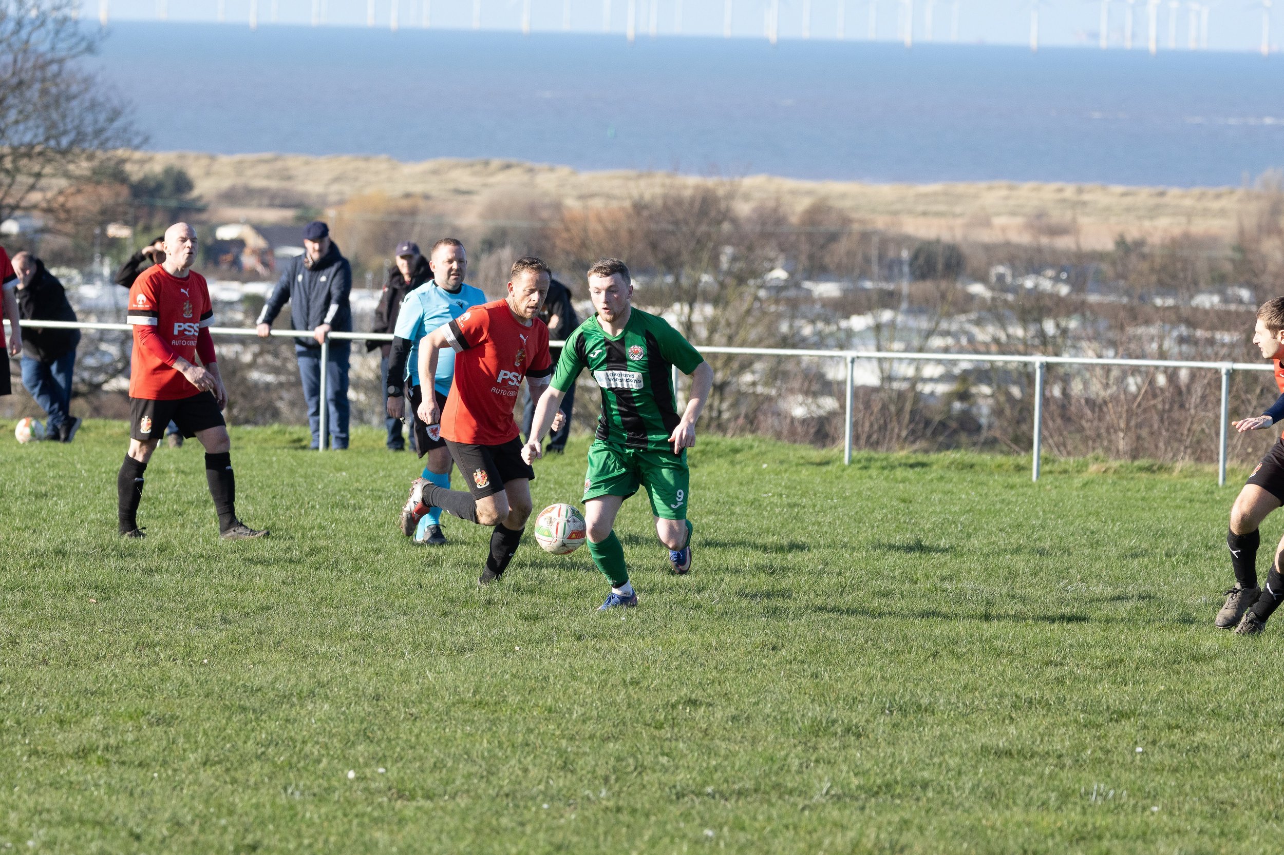 Soccer players in red and green uniforms competing for the ball on a grassy field.